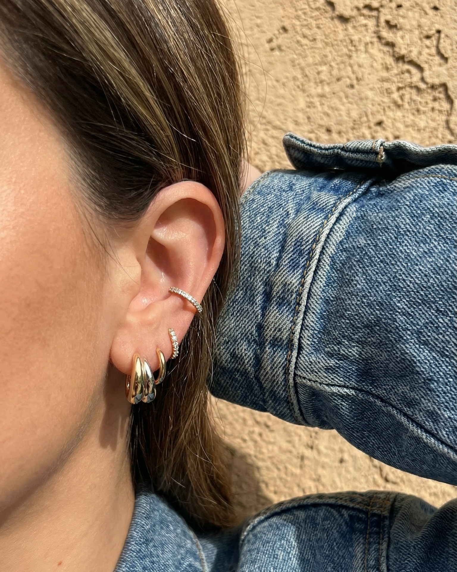 Close-up of a person wearing hoop earrings with a denim jacket and sand background