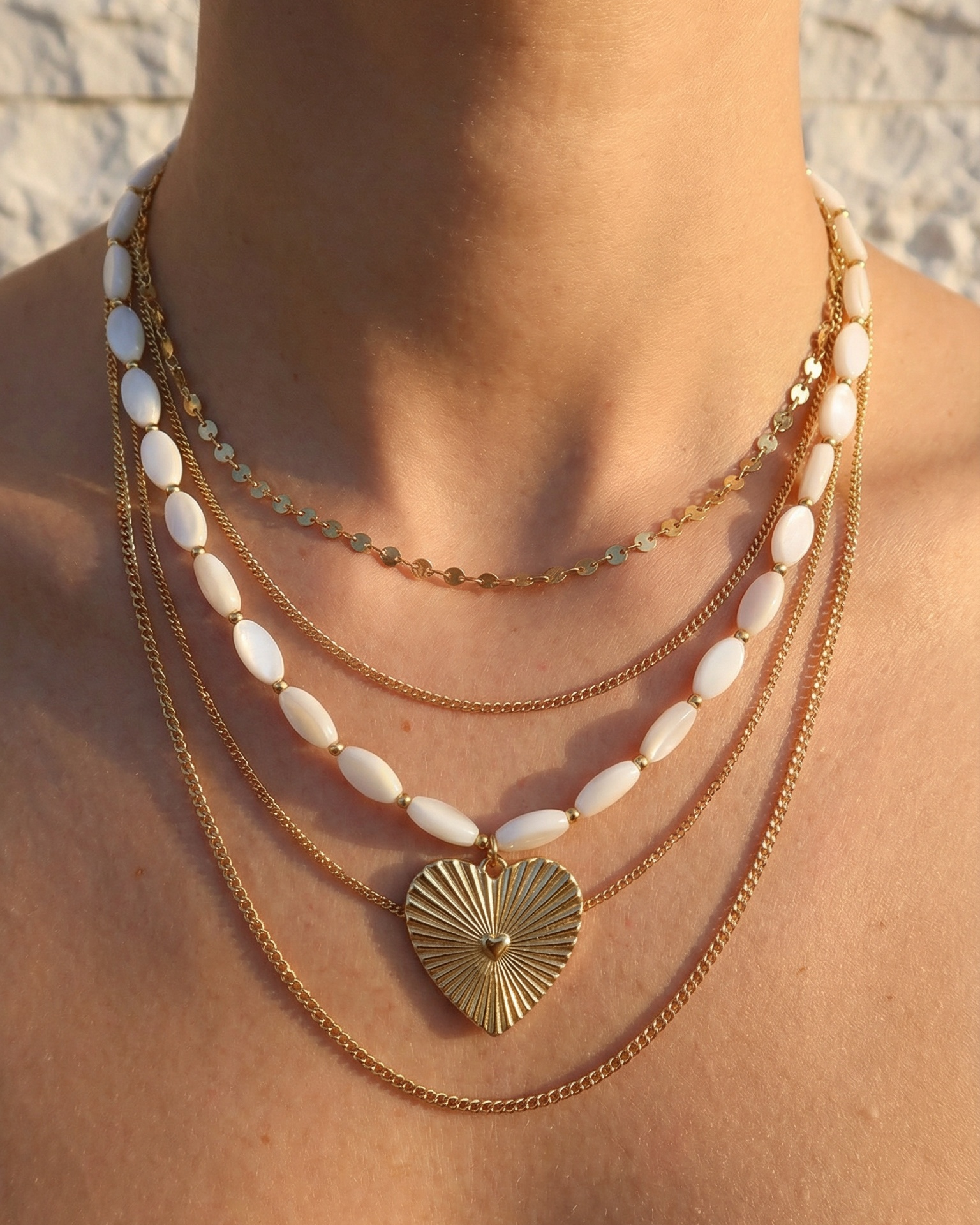 Necklace with shell pendant and gold chain on a person against a blurred natural background
