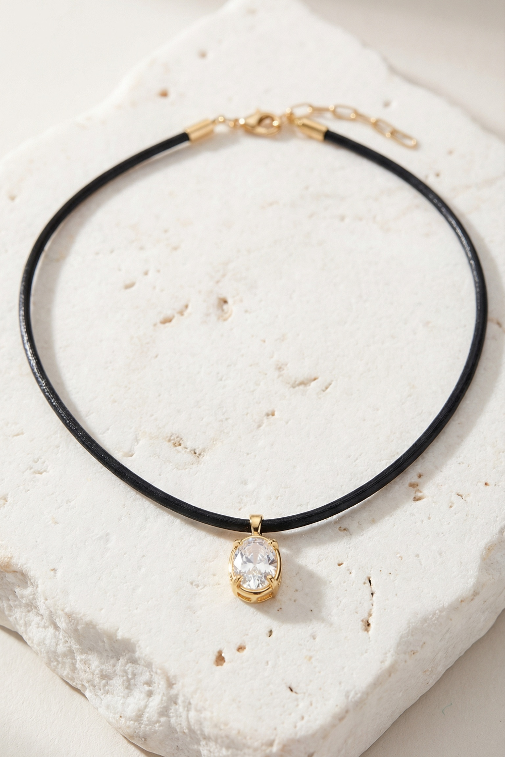 Minimal black cord necklace featuring a gold oval stone pendant on neutral textured background
