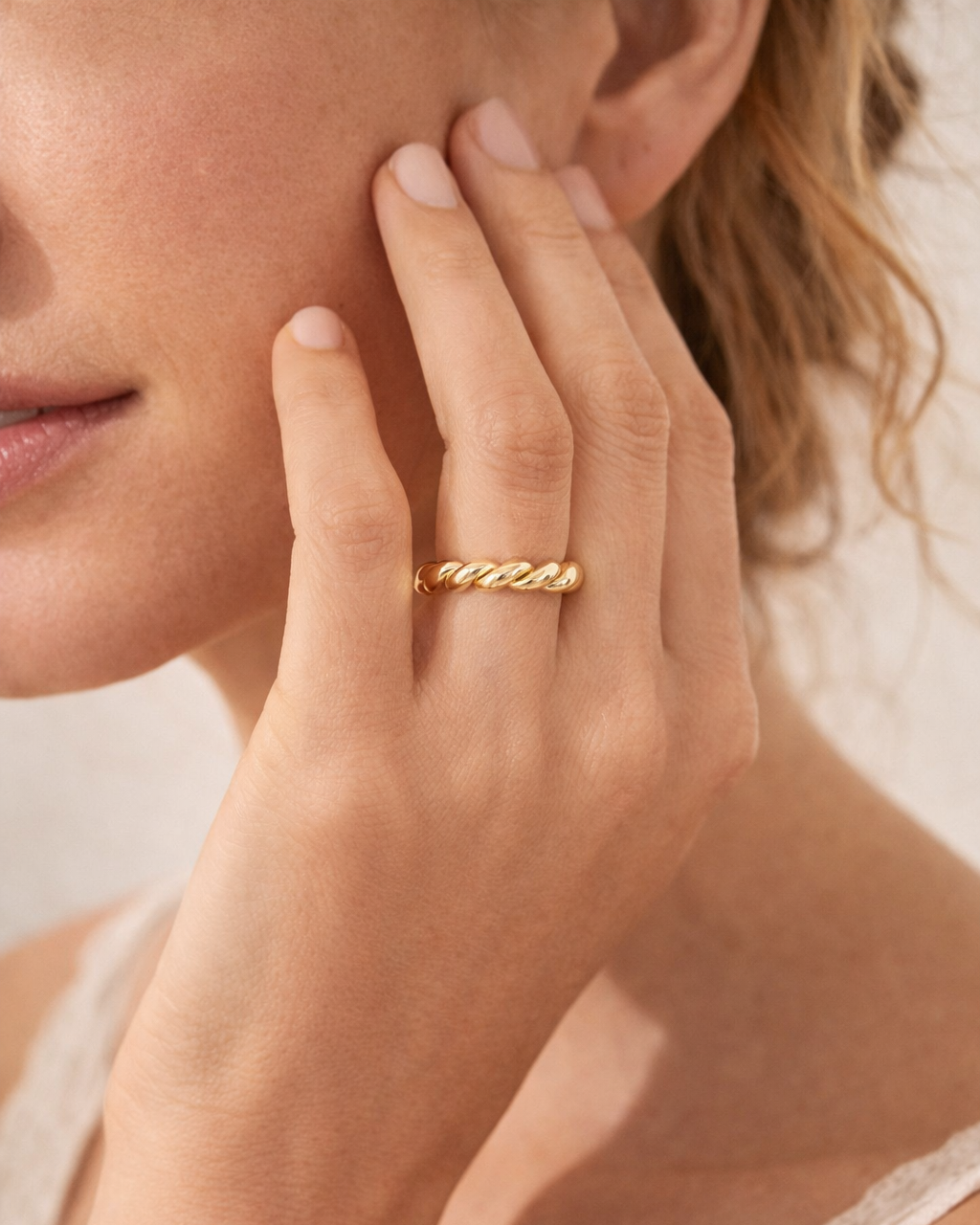 Close-up of a hand wearing a gold twist band stacking ring with a blurred background