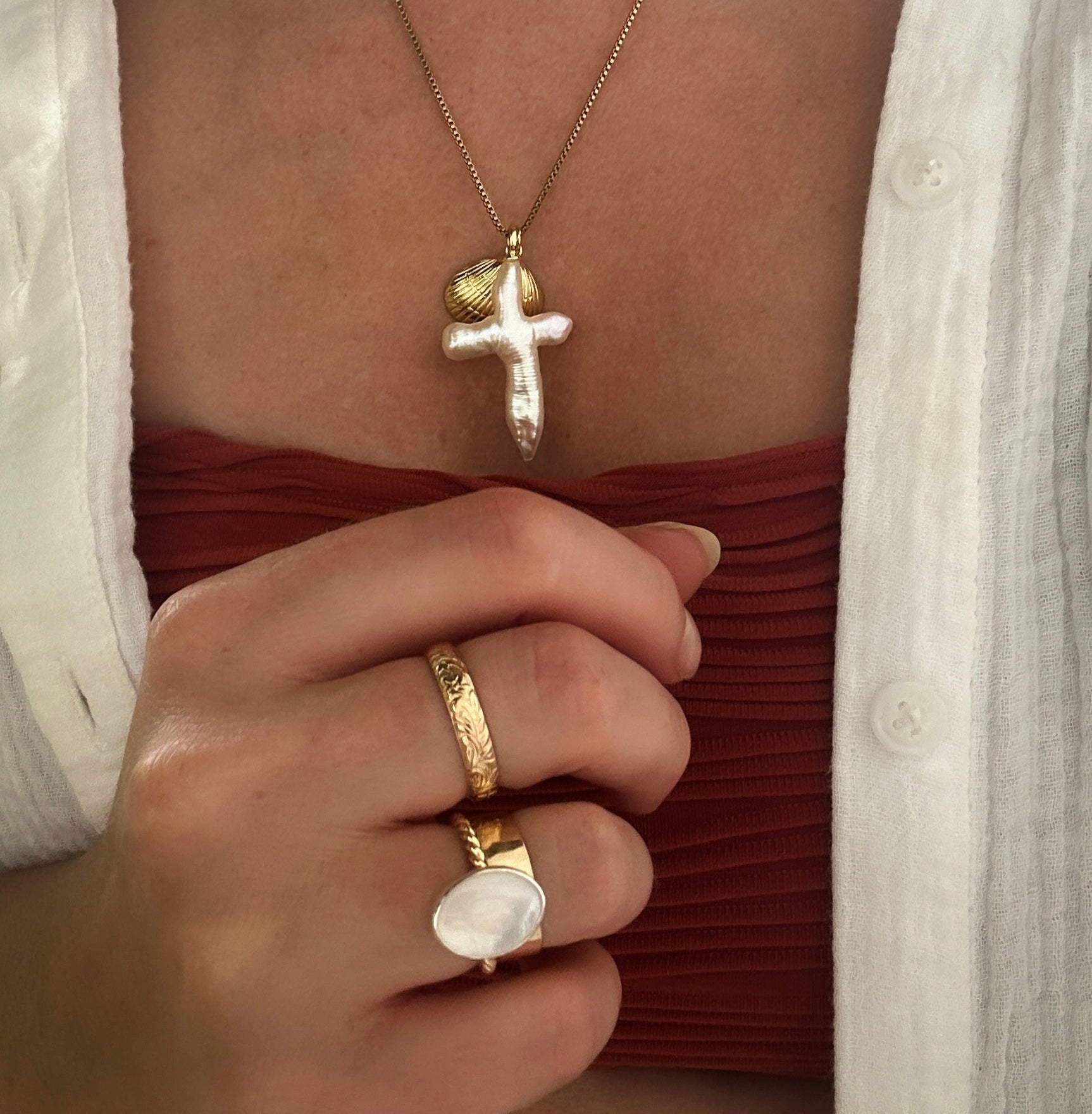 Close-up of a person wearing a gold necklace with a cross pendant and a matching ring.