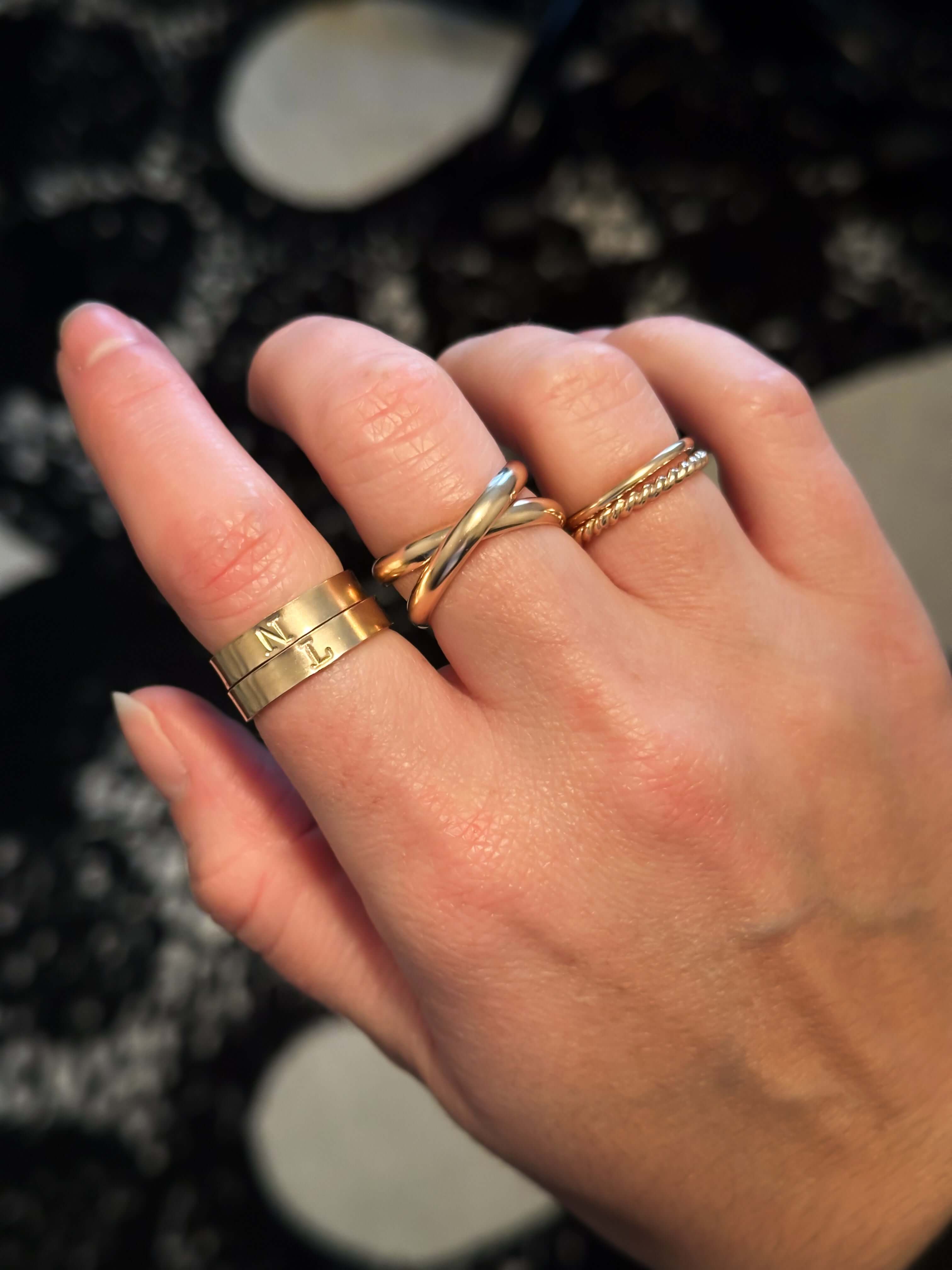 A hand wearing three rings: an Initial Band, a twisted gold ring, and a thin 14k gold filled band.
