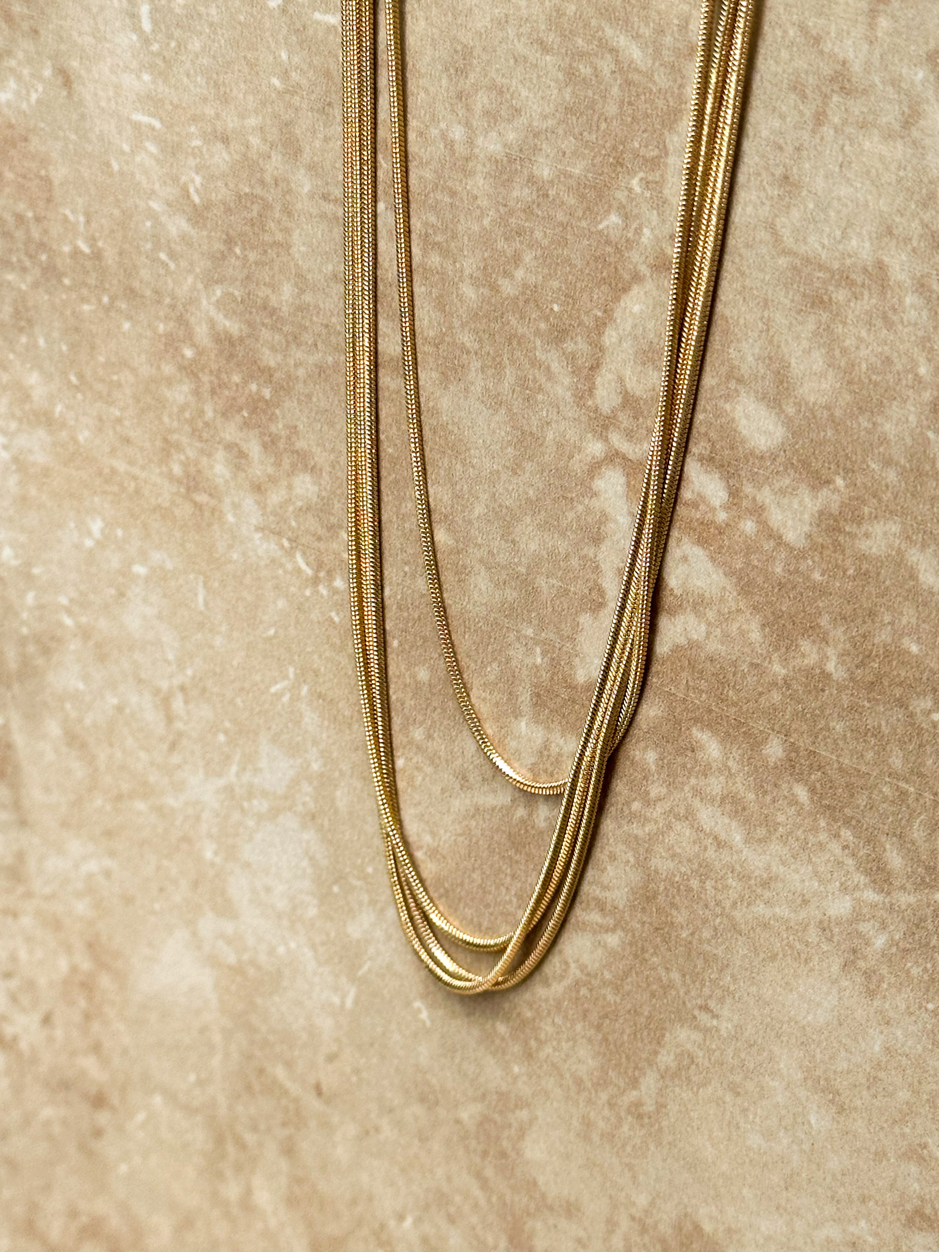 Gold layered necklaces against a textured beige background.