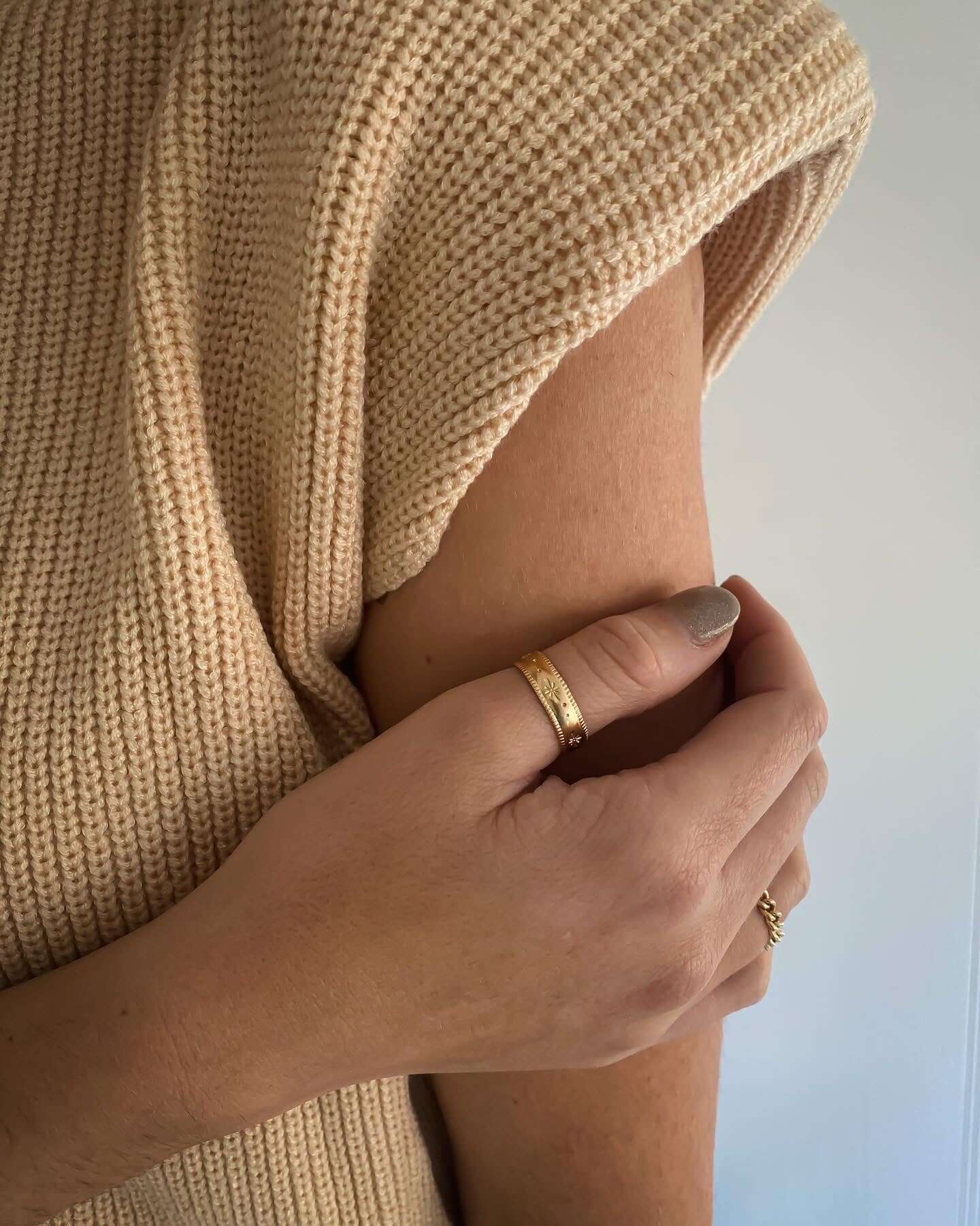 Close-up of a person wearing a beige knitted top, showing their hand adorned with celestial jewelry, including the stunning Stardust Ring in 14k gold fill.
