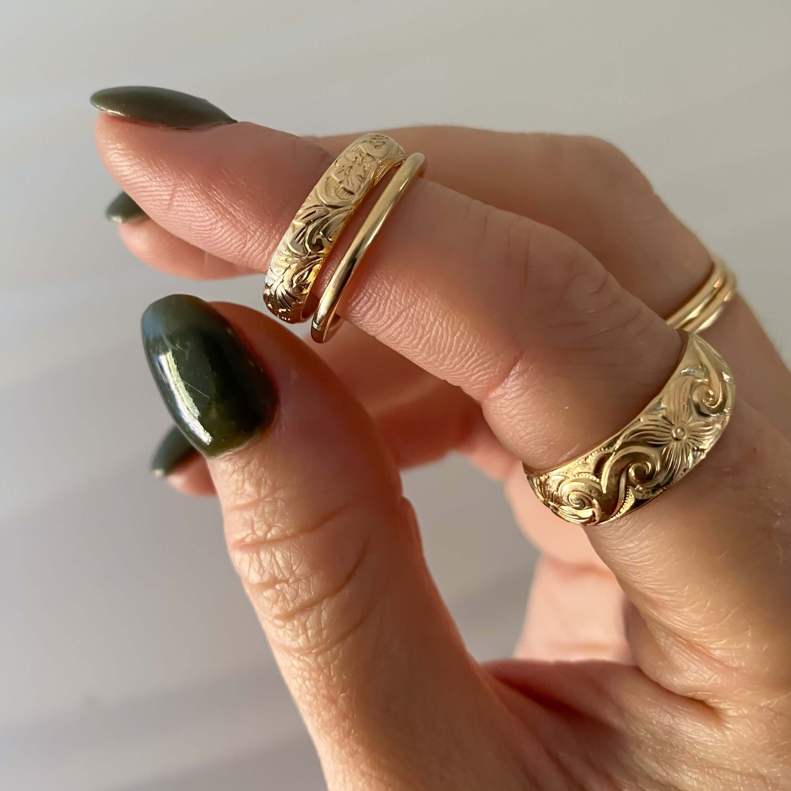 A hand with green-painted nails adorned with the Floral Ring Set, featuring engraved gold rings and a vintage floral charm on the thumb, index, and middle fingers.