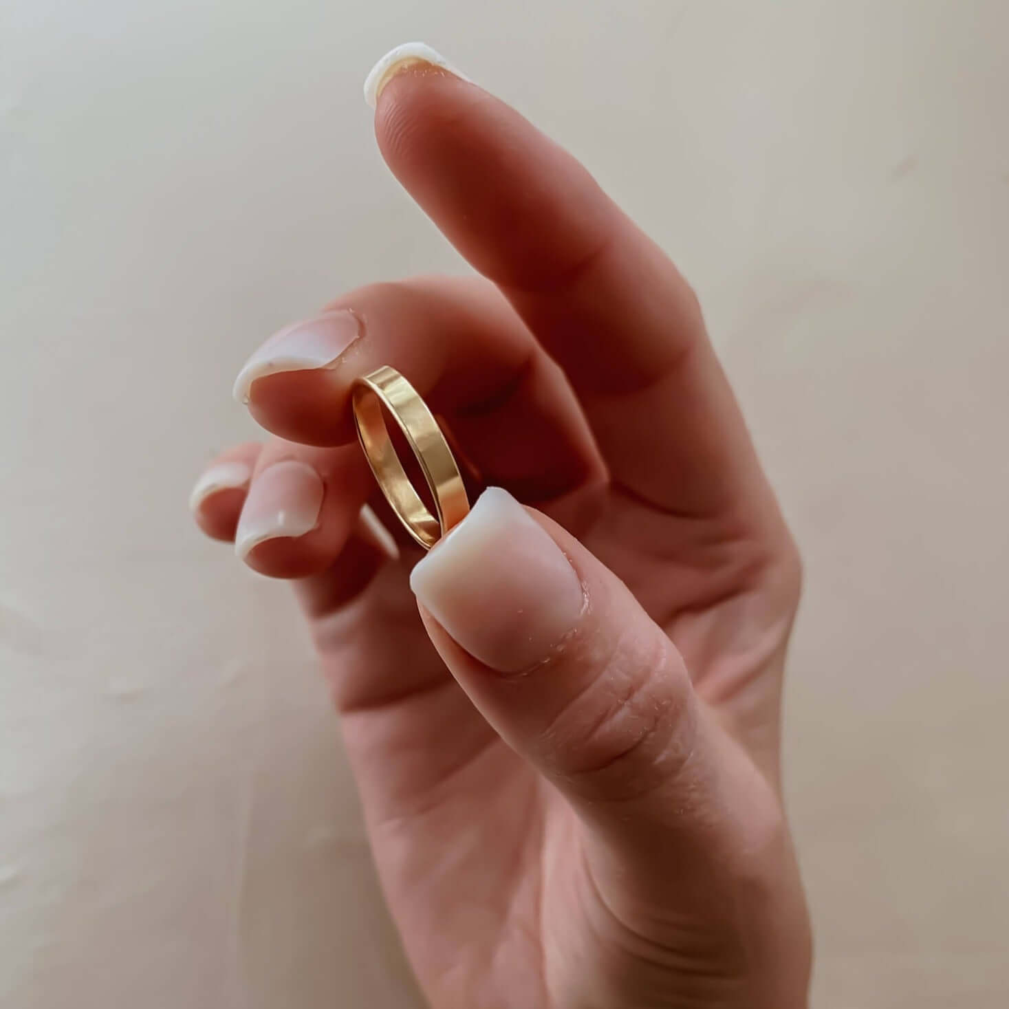 A hand holds the 3 mm Everyday Gold Ring between the thumb and index finger against a neutral background.