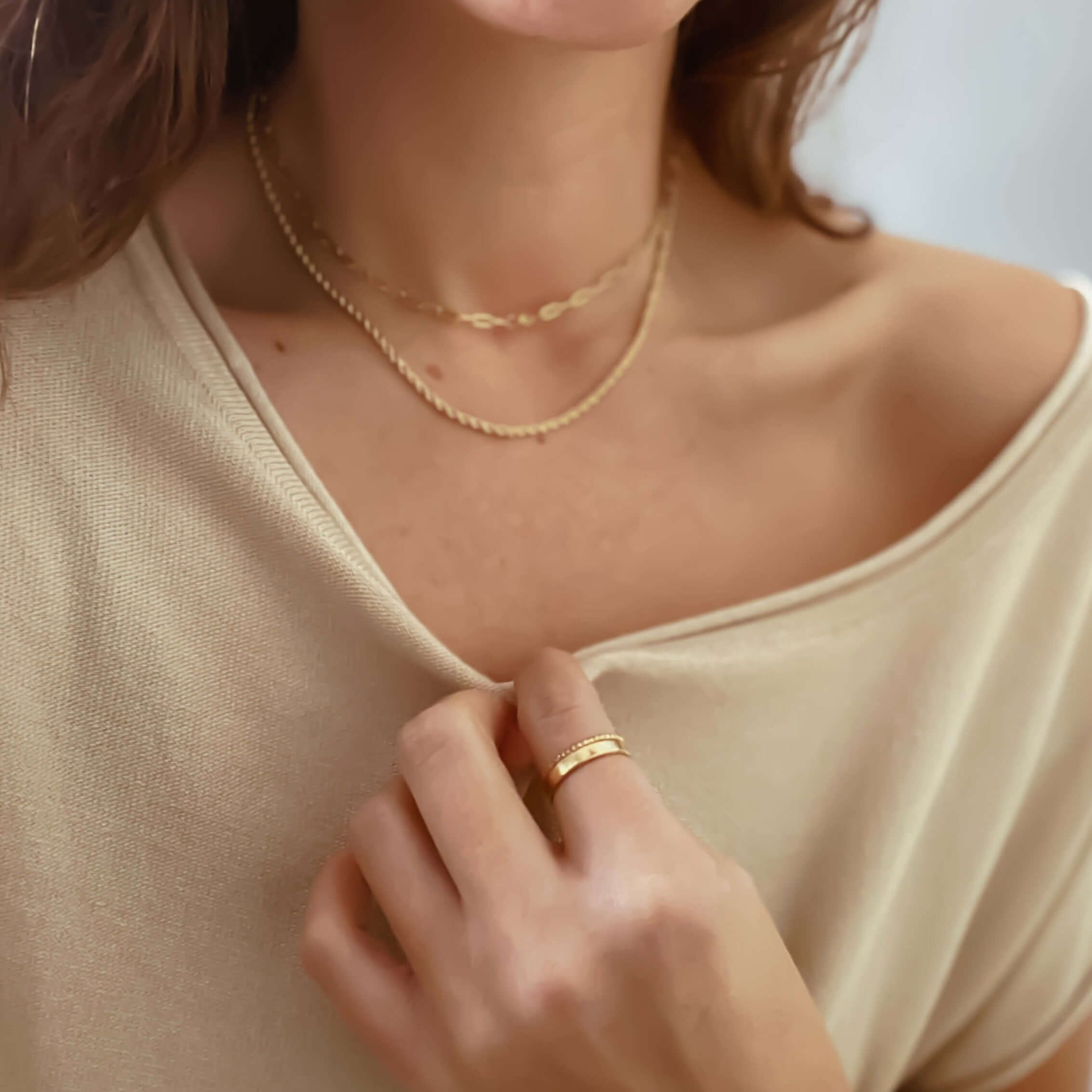 Person wearing layered gold necklaces and a versatile 3 mm Everyday Gold Ring, holding the collar of a beige off-the-shoulder top.