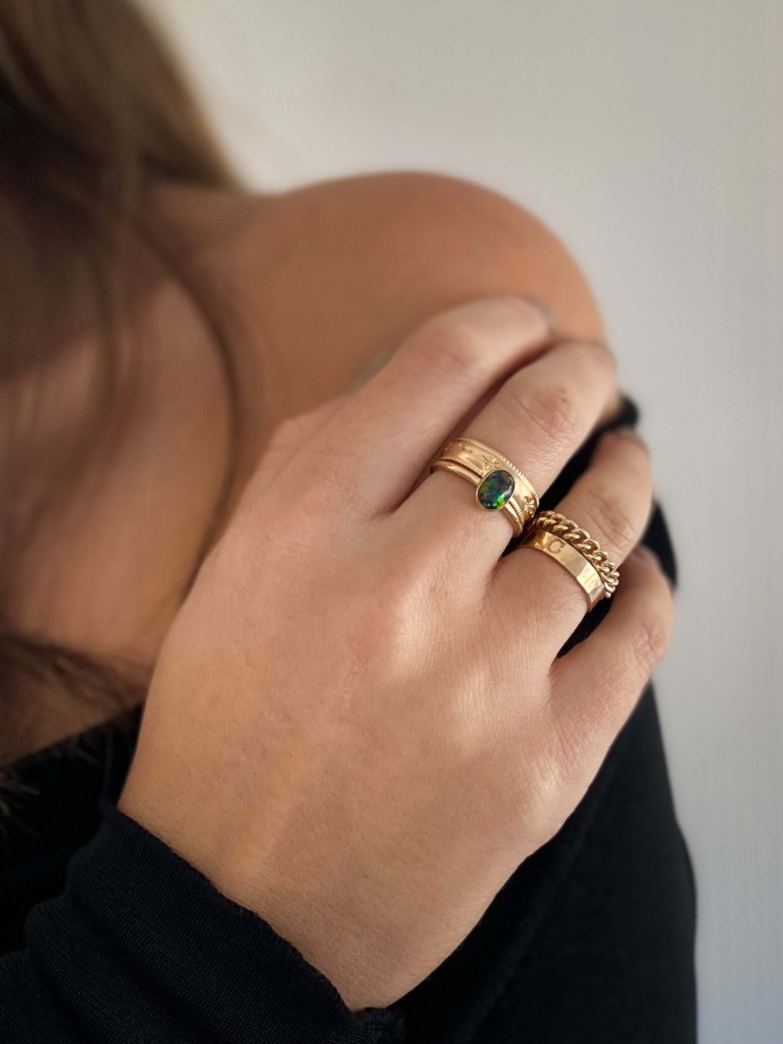 Close-up of a woman's hand adorned with celestial jewelry, featuring gold rings—one set with a green stone and the other as the delicate **Stardust Ring** in 14k gold fill—resting gracefully on her shoulder.
