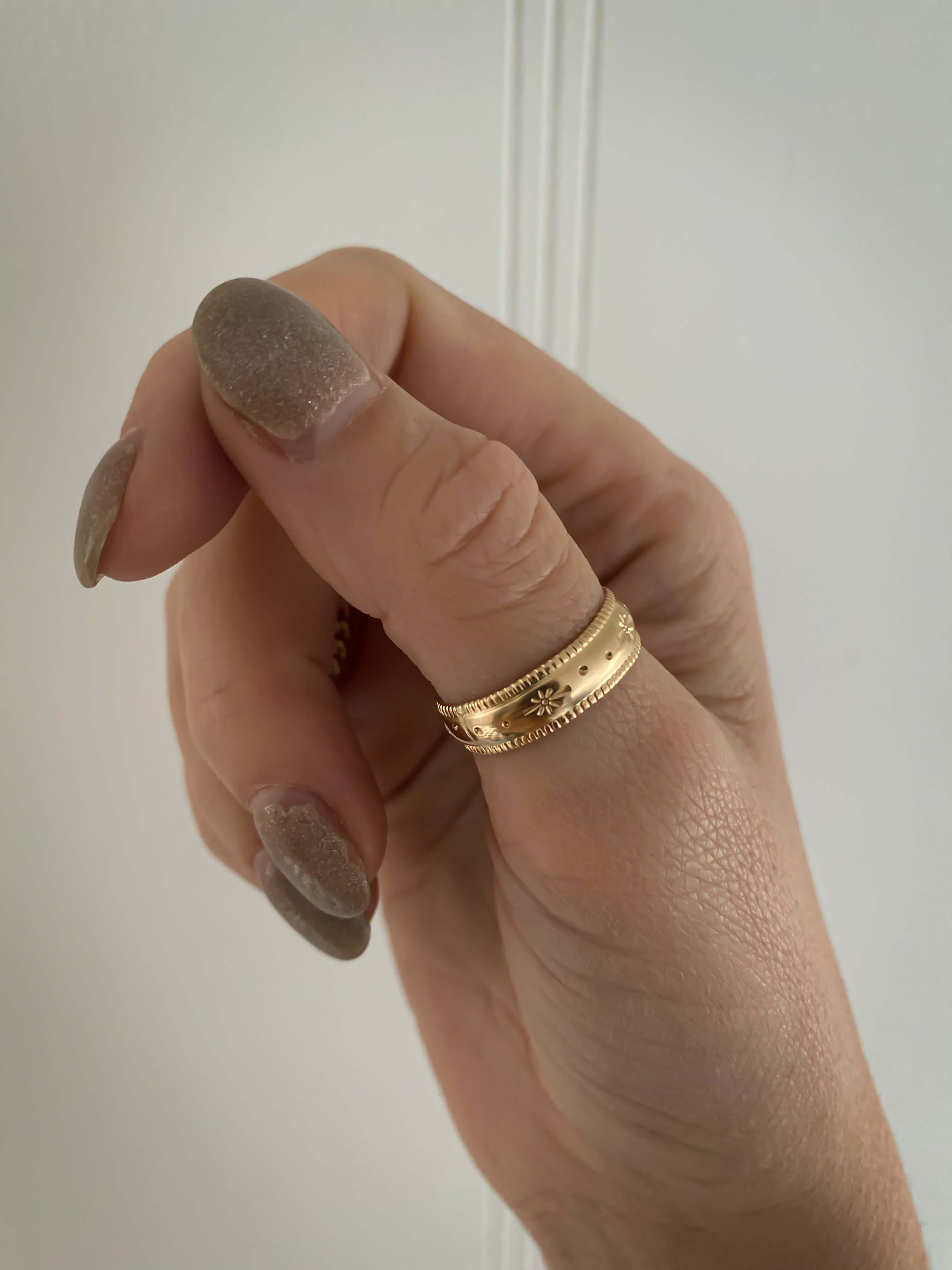 A hand with beige nails wearing the Stardust Ring, meticulously crafted from 14k gold fill and featuring intricate celestial jewelry details.