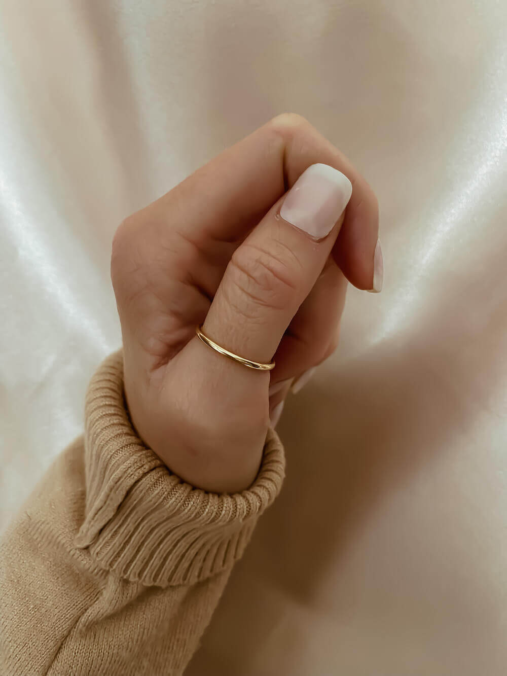 A hand wearing the Simple Gold Band, with a beige sleeve visible, is shown against a light background.