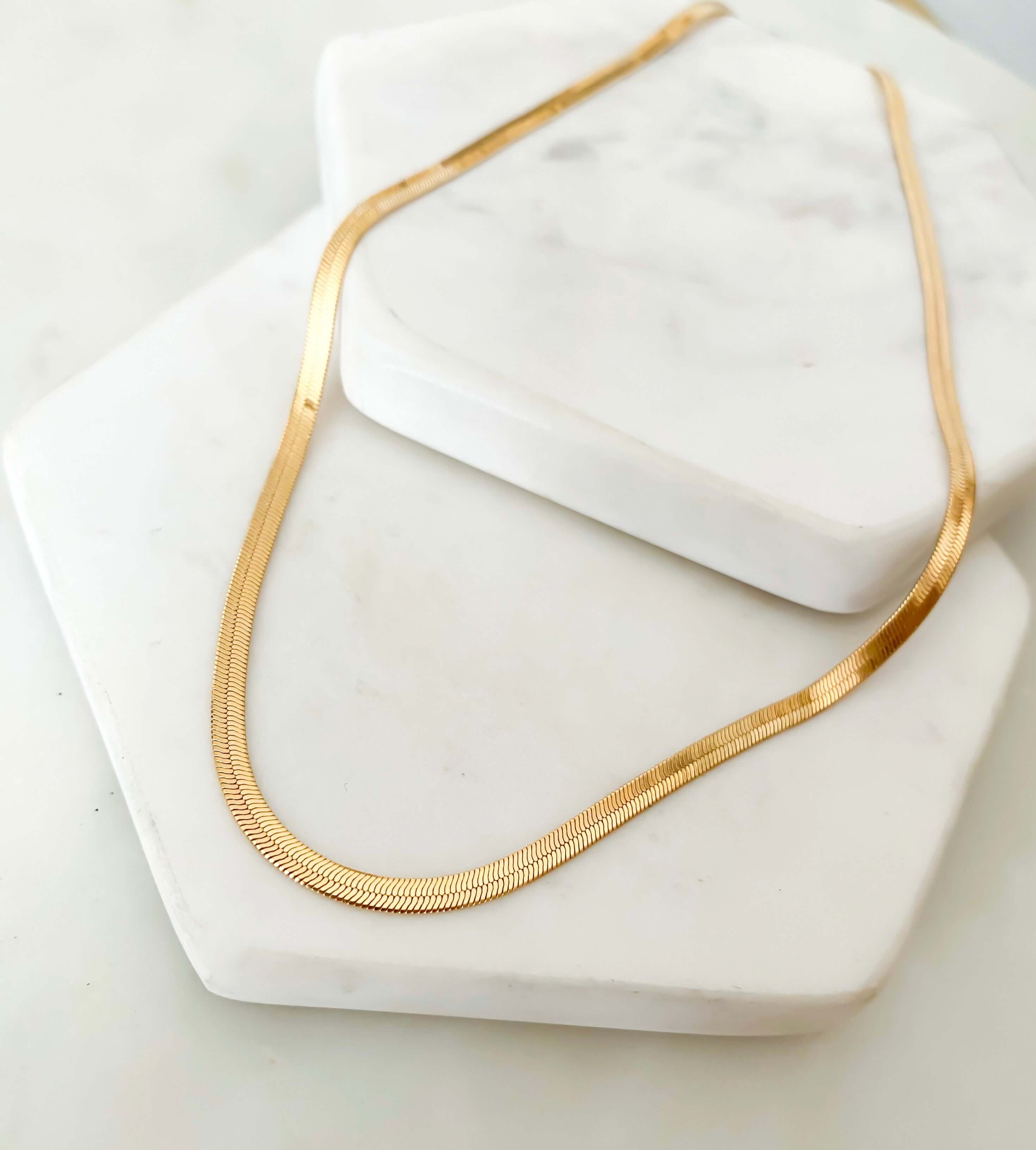 A chic *Selena Chain Necklace* is elegantly showcased on white, marble hexagon slabs, highlighting its stylish design and ready-to-ship convenience.