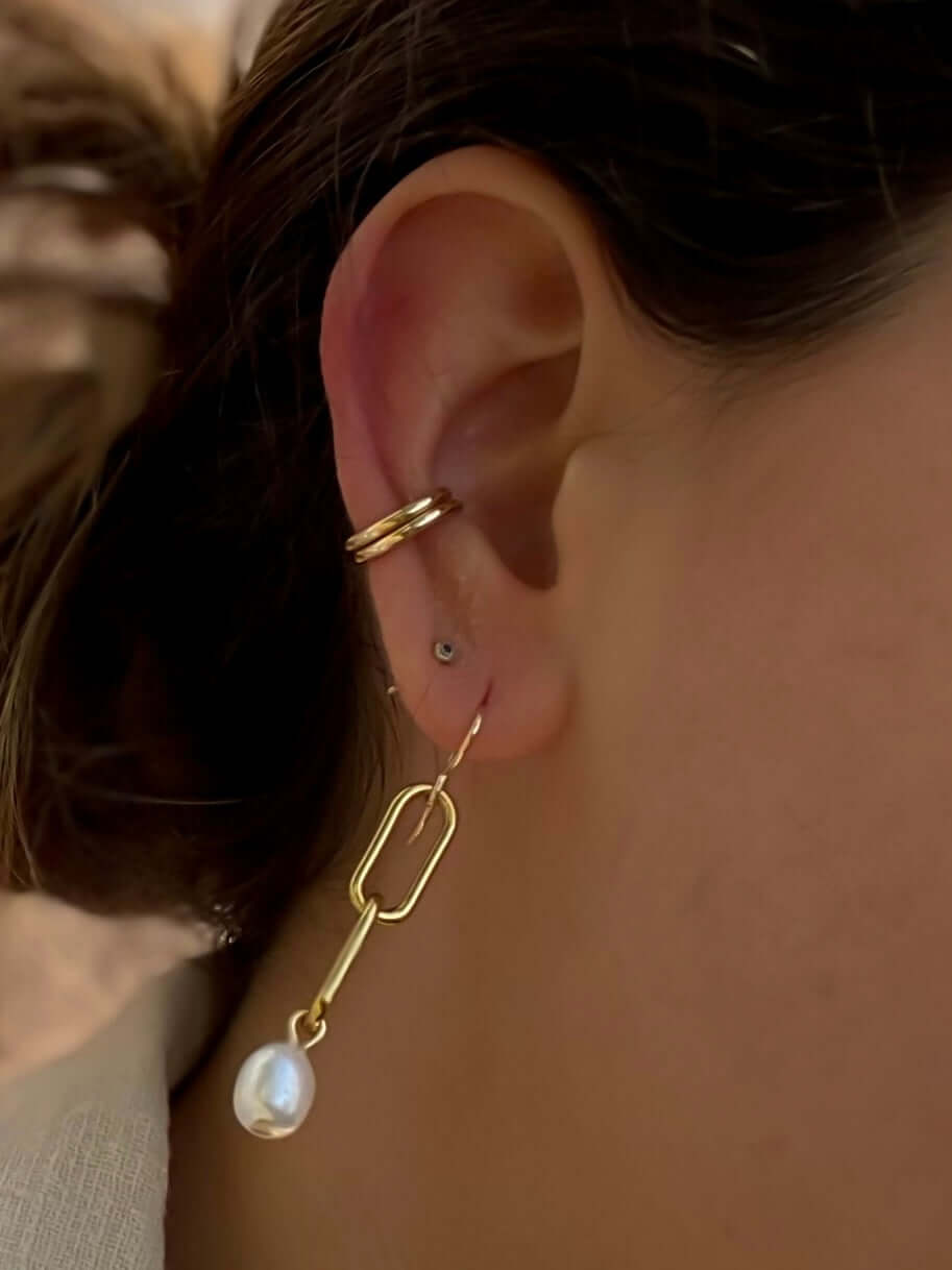 Close-up of a person's ear adorned with a gold earring featuring a rectangular link and a dangling pearl, complemented by three small hoop earrings and the elegant Everyday Ear Cuff.