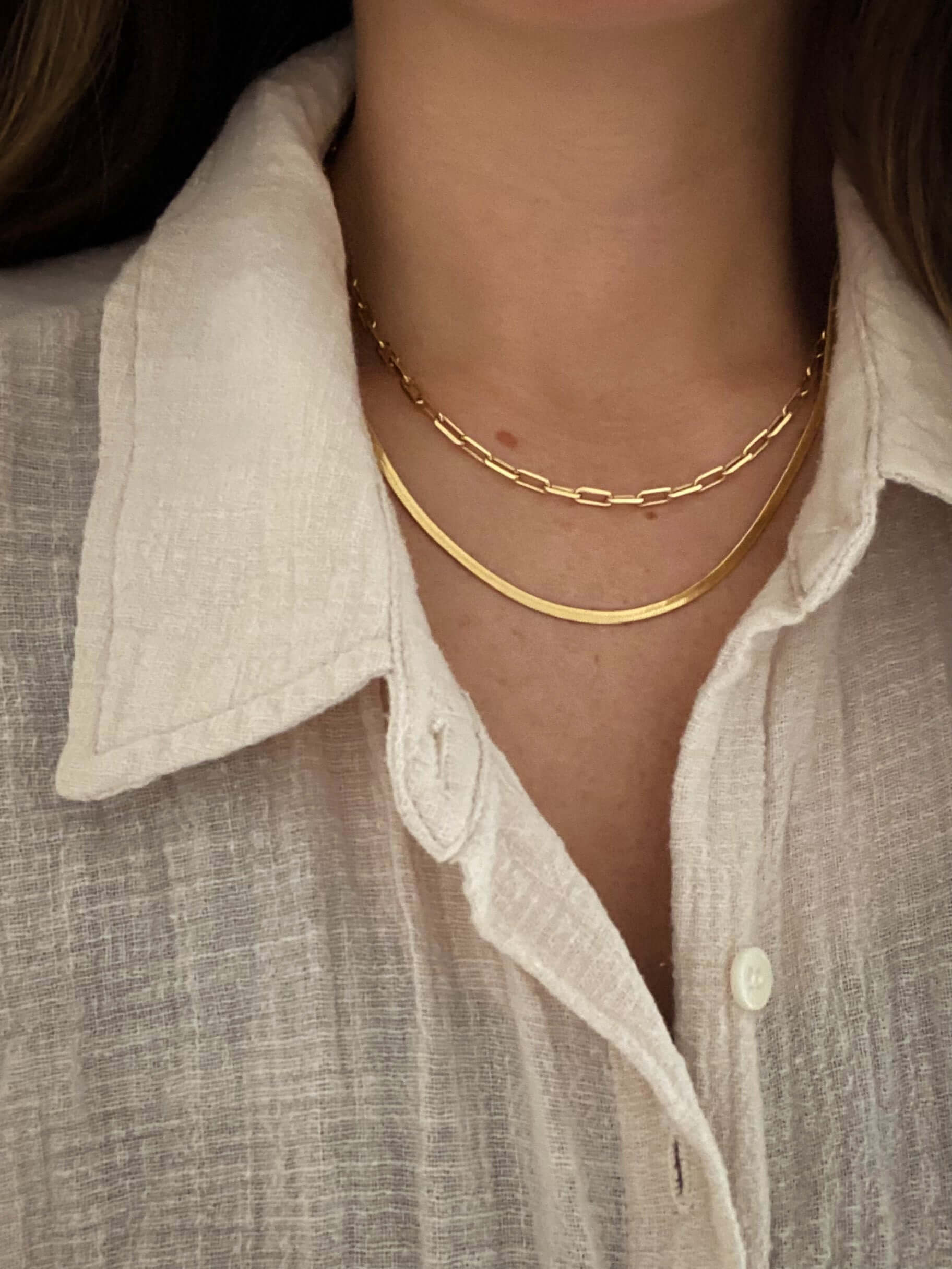 Person wearing a textured white collared shirt and two chic necklaces: one with a curved bar and the other, a Selena Chain Necklace of gold links.