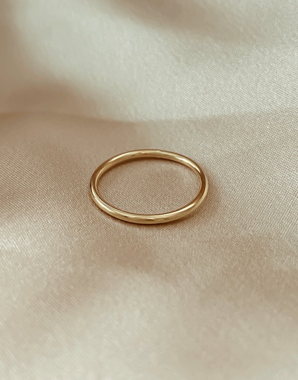The Simple Gold Band rests elegantly on smooth, cream-colored fabric, making it perfect for stacking or wearing solo.