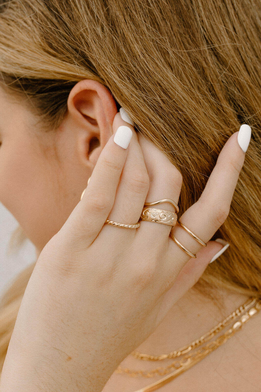 Close-up of a person touching their blonde hair, adorned with multiple Peak Rings crafted from 14k gold fill, and showcasing white nail polish.