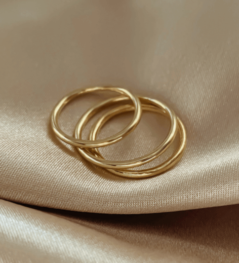 Three elegant, made-to-order Simple Gold Bands rest on a swath of shimmering beige satin fabric.