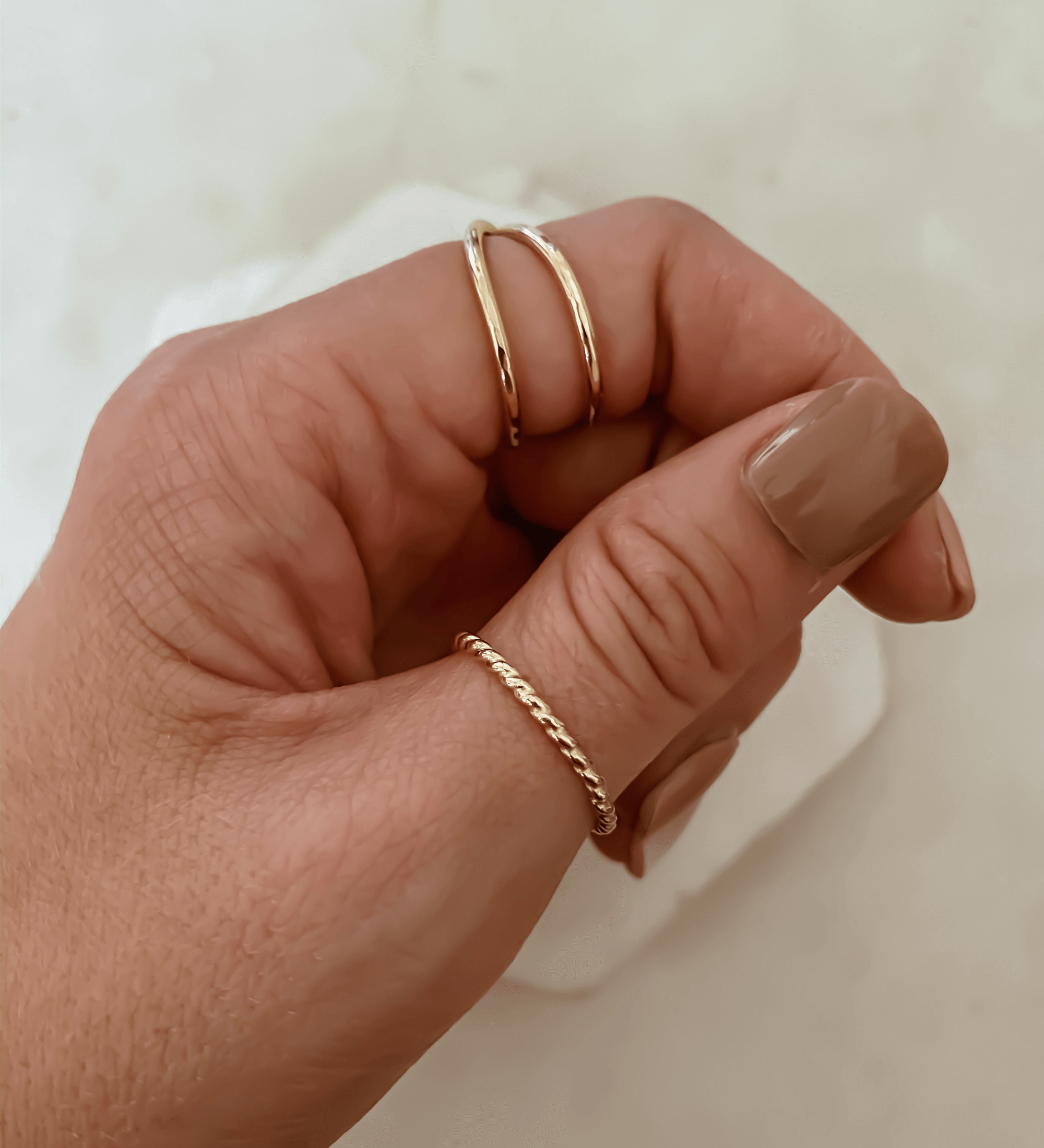 Close-up of a hand wearing two 14k gold filled Thin Twist Bands, one on the thumb and another stacking ring on the index finger, both complementing the neutral-colored nail polish.