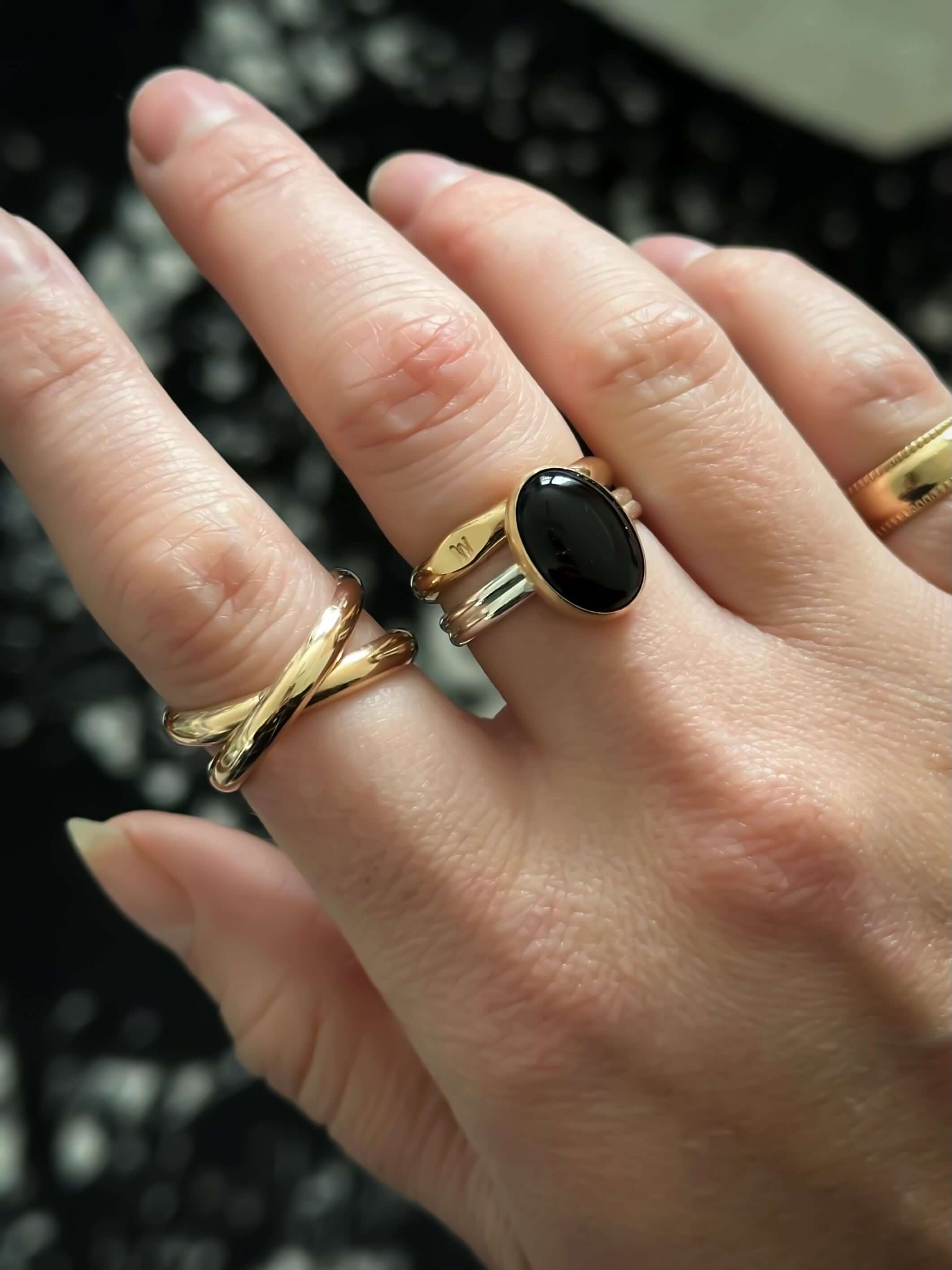 Close-up of a hand adorned with multiple rings, including a black oval stone ring and a Crossover Ring, achieving a chunky look.