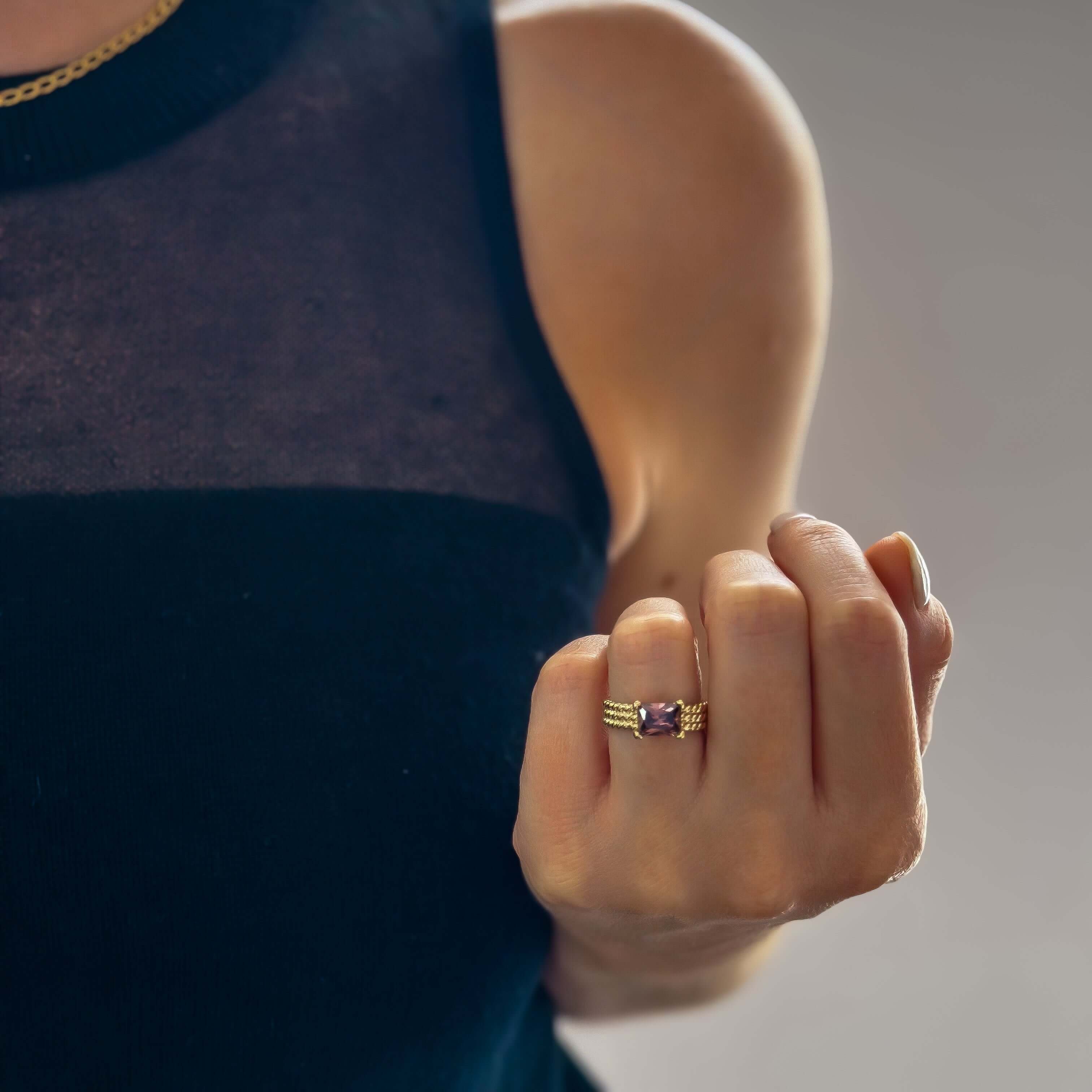 Person wearing a black sleeveless top showcasing the Ivy Ring - Magenta with a gold band and magenta gemstone on their index finger.