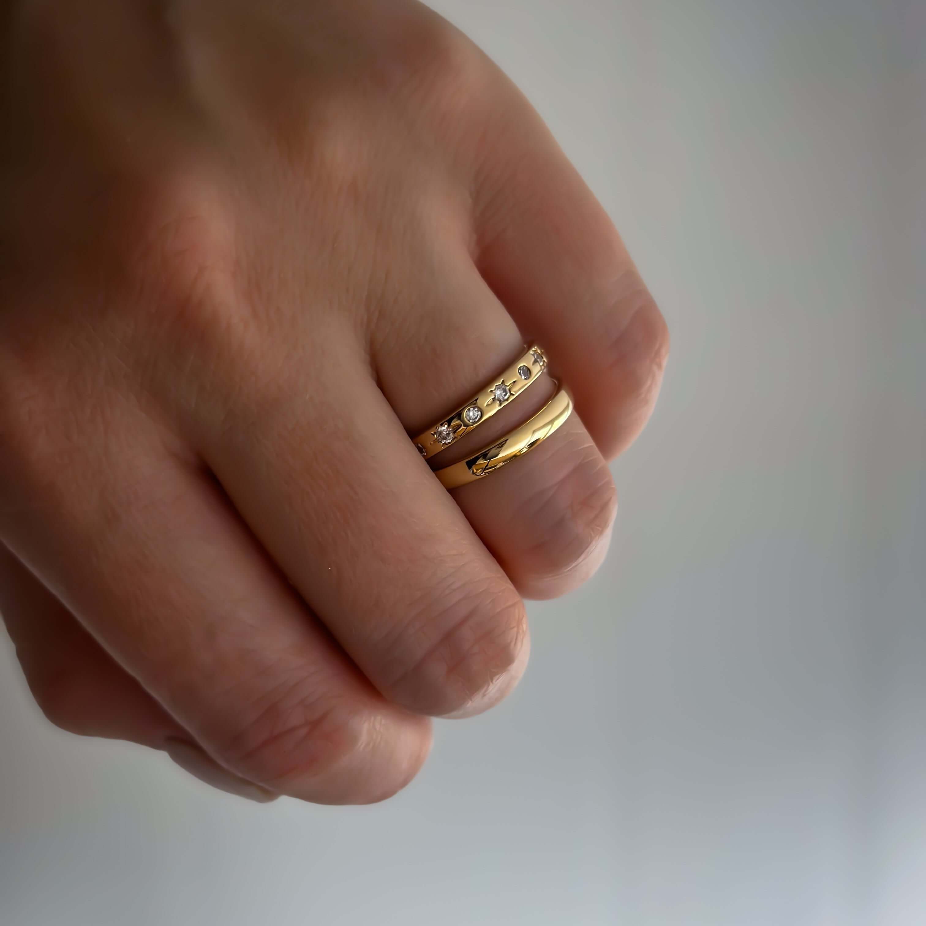 Close-up of a hand adorned with two Astraea Rings, featuring 18k gold plating and sparkling CZ stones on the ring finger.