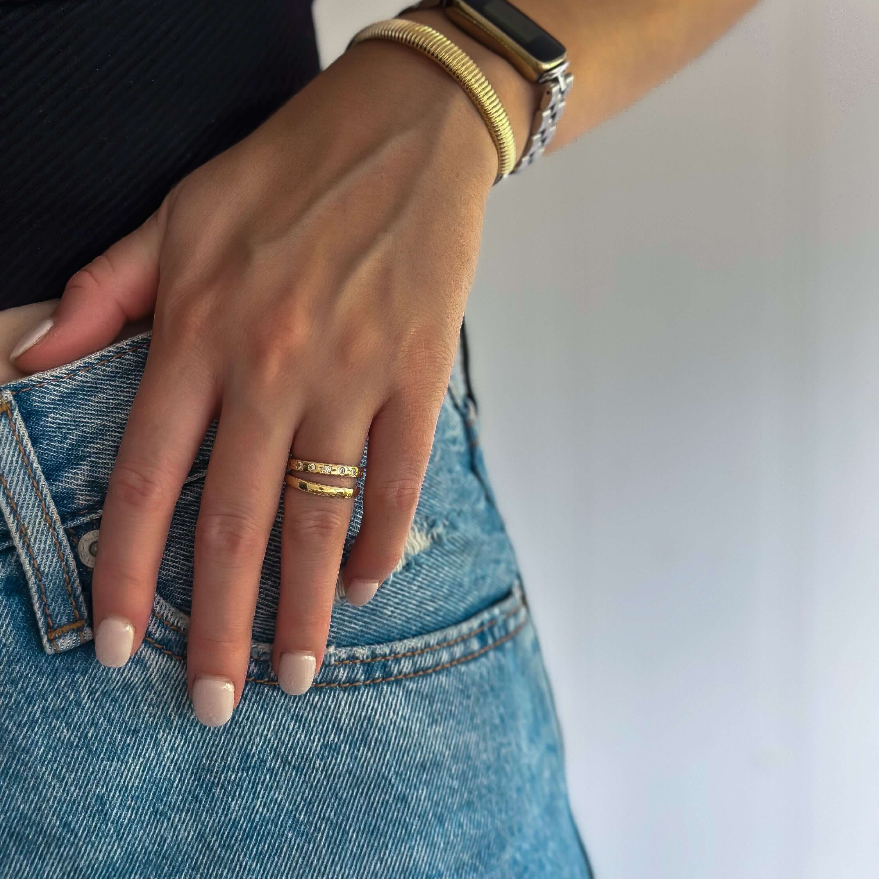 Close-up of a hand resting on a hip wearing denim jeans, adorned with the Astraea Ring, a gold bracelet with 18k gold plating, and a smartwatch.