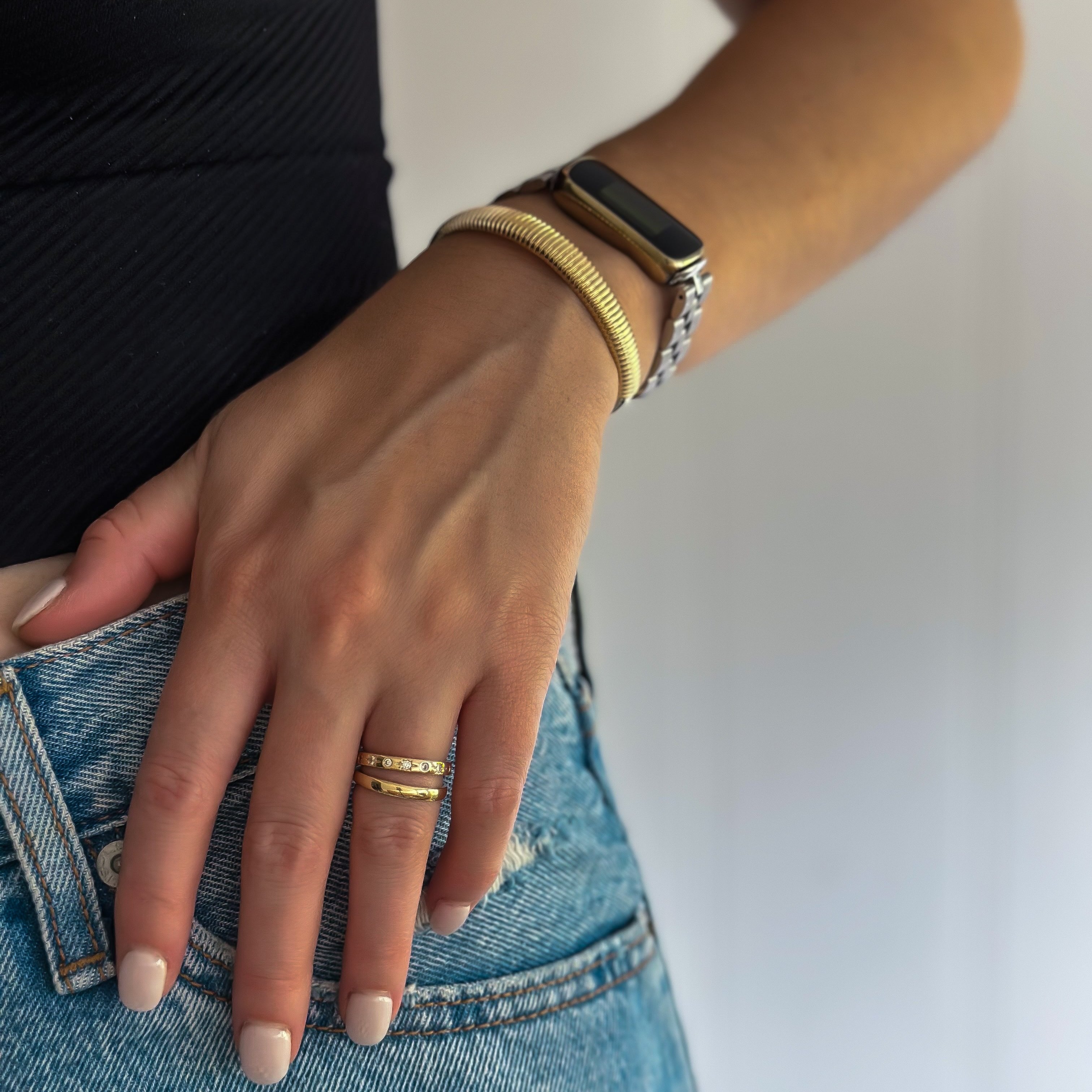 Close-up of a hand adorned with a gold watch, rings, and the Venice Cuff Bracelet featuring unique texture and 18k gold plating, resting on the pocket of blue jeans.