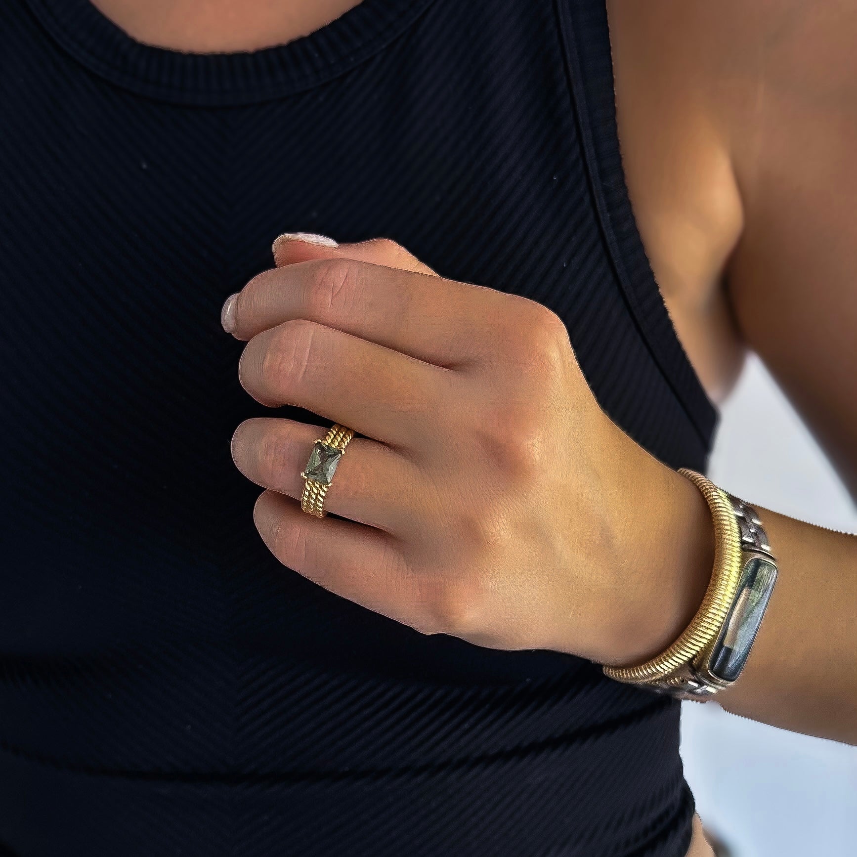 A person wearing a black sleeveless top, a gold ring, and a watch with a gold and silver band complemented their look with the distinctive texture of the Venice Cuff Bracelet adorned in 18k gold plating.