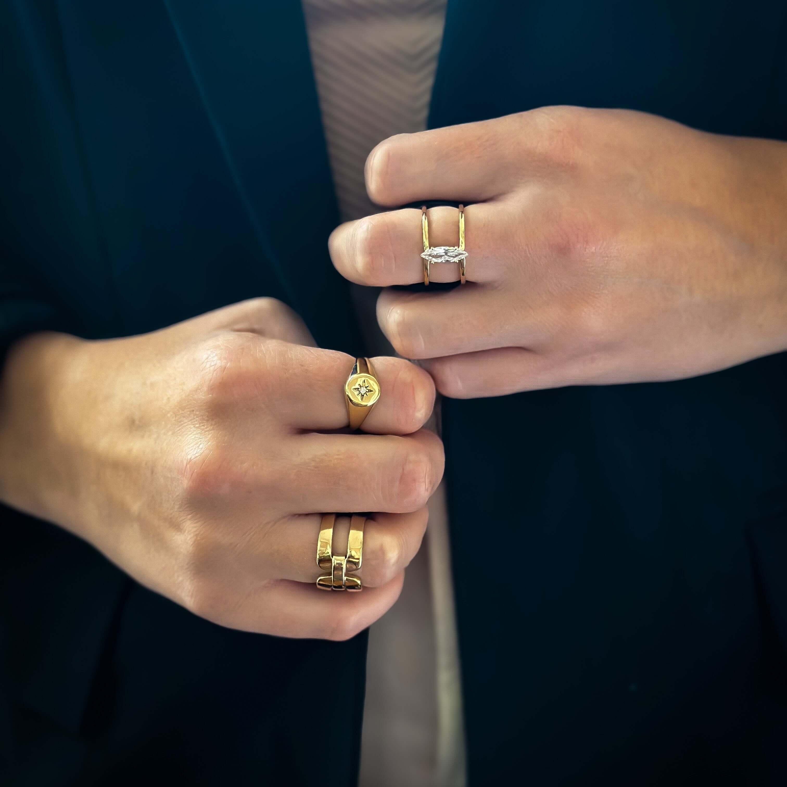 Close-up of hands adorned with multiple gold rings, featuring the Double Buckle Ring with 18k gold plating and a stunning diamond, all set against a dark background.