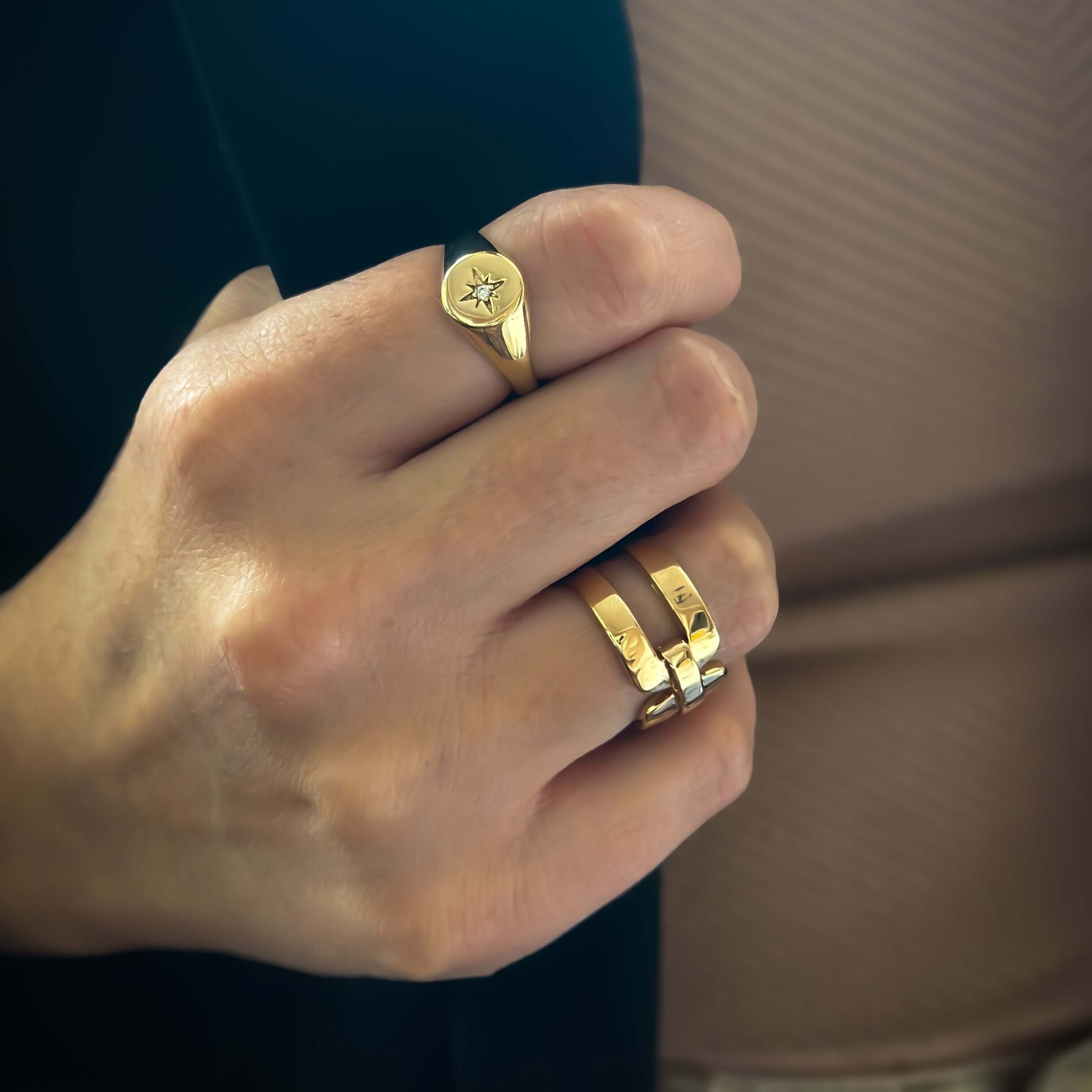 Close-up of a person wearing multiple 18k gold-plated rings on their fingers, with a unique star design on one ring and the Double Buckle Ring adding to the elegance.