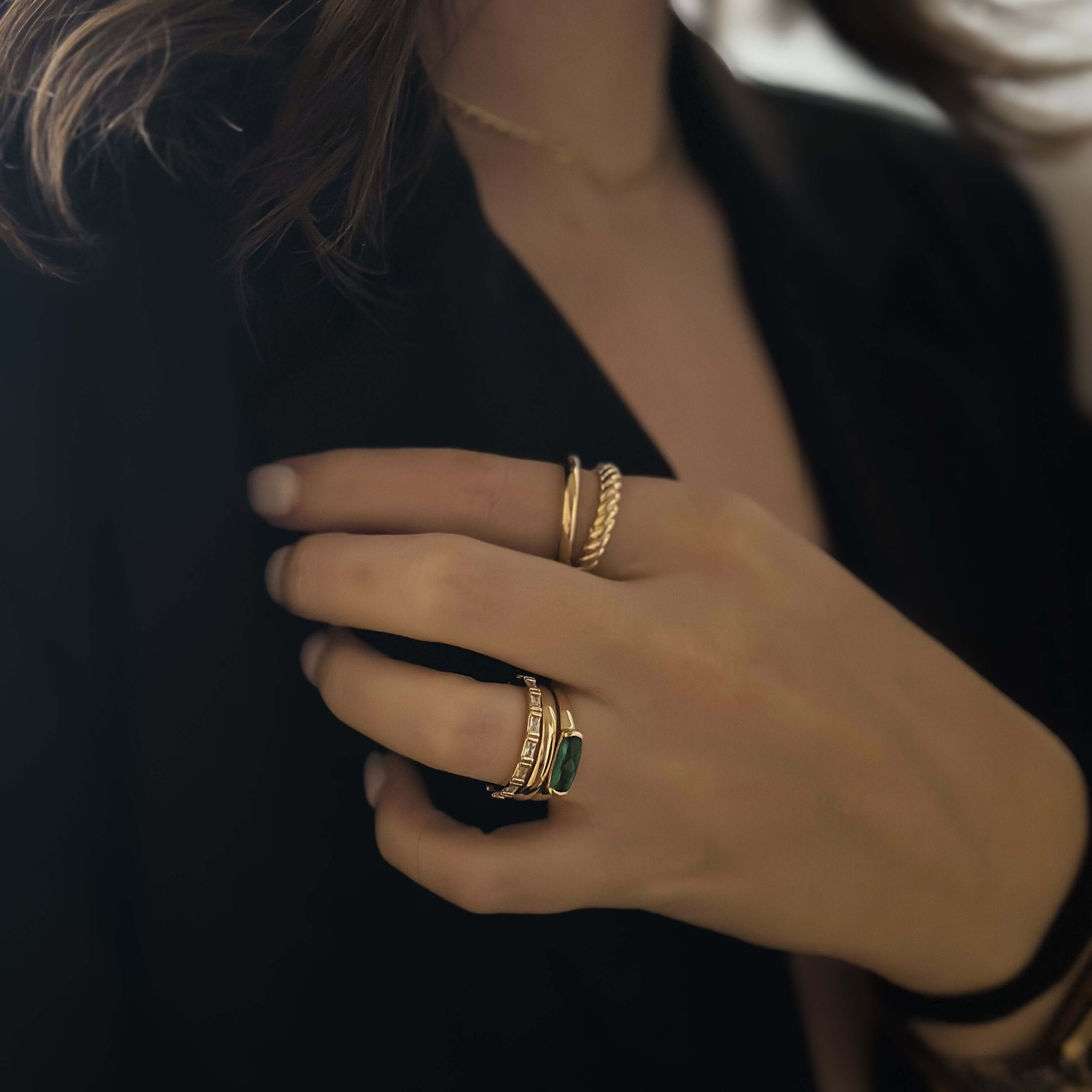 Close-up of a person gently touching their chest, wearing multiple stylish rings, with the elegant and bold Diana Double Ring standing out and dressed in a black blazer.