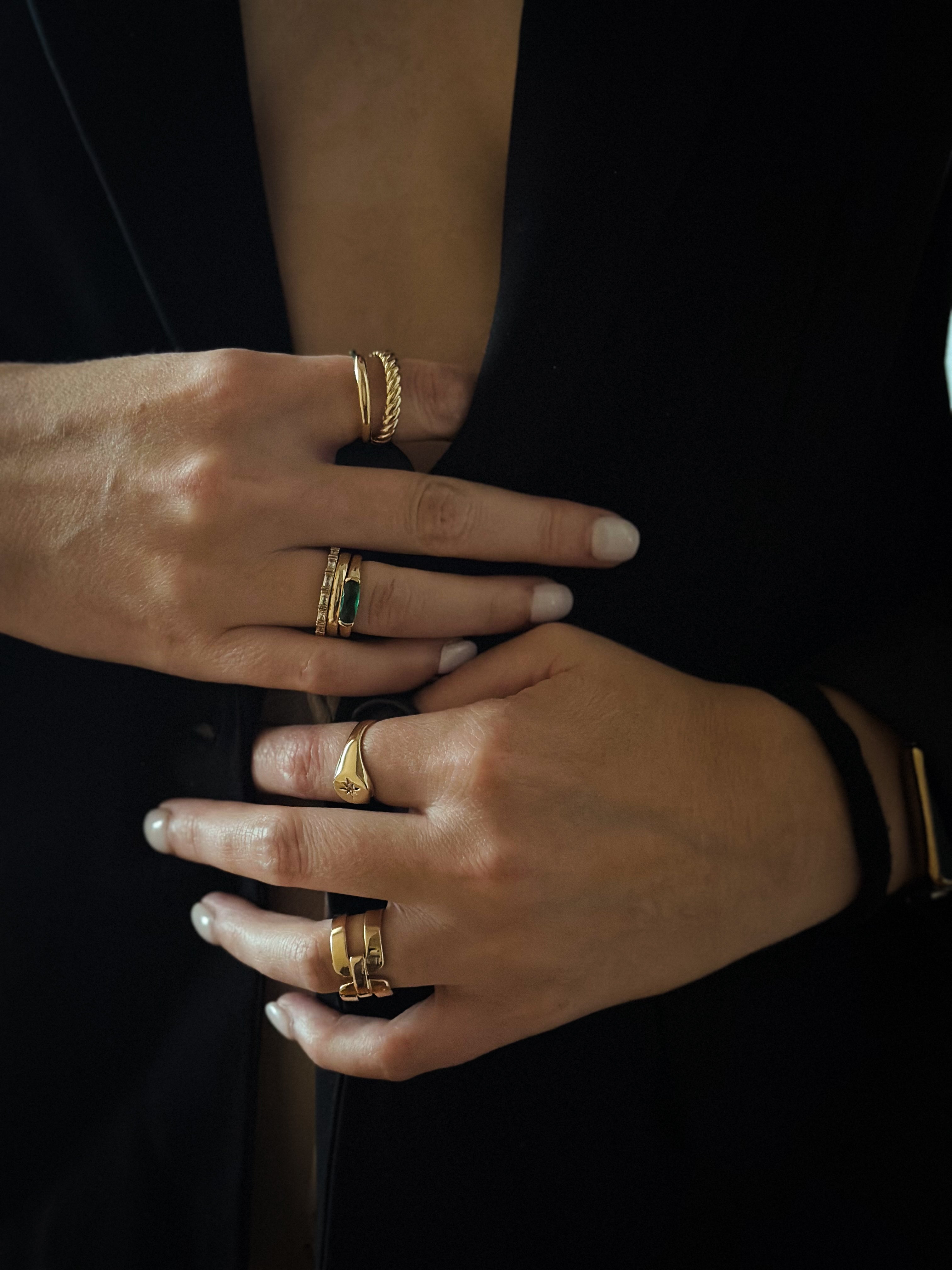 Close-up of a person wearing multiple gold rings on both hands, dressed in a black garment.