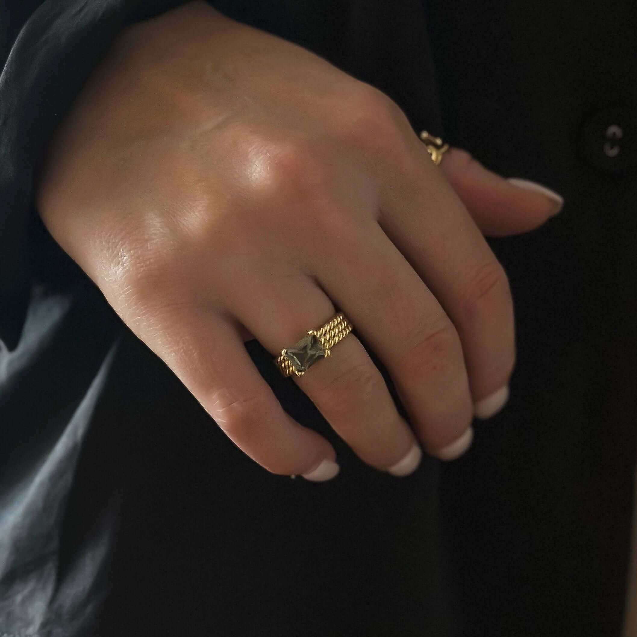 Close-up of a hand wearing the Ivy Ring - Olive Smoke, showcasing its elegant triple-twist gold band with an olive smoke stone, set against a dark background.