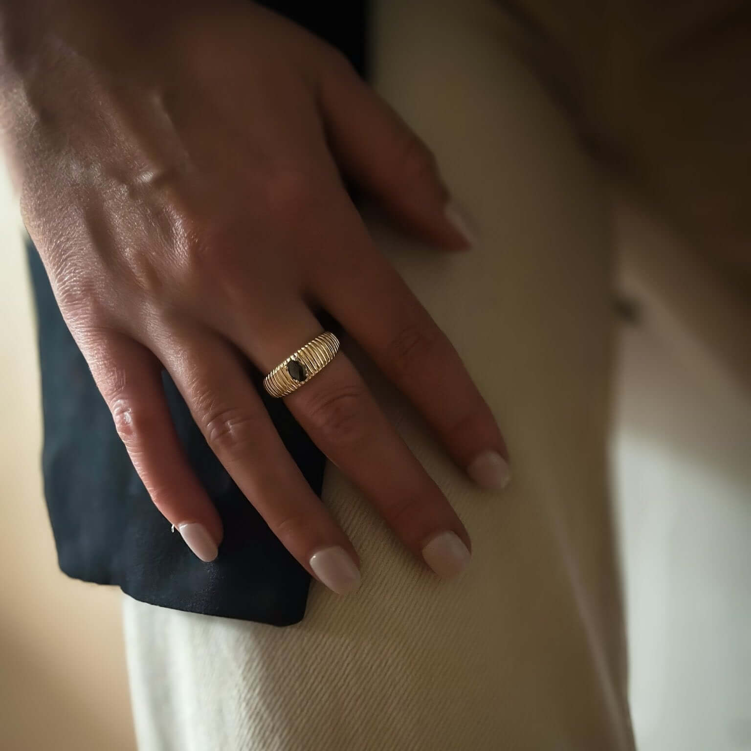 Close-up of a hand adorned with the Venice Ring - Onyx, resting on a knee clad in light-colored pants and dark fabric, exuding Venetian chic and Italian glamour.