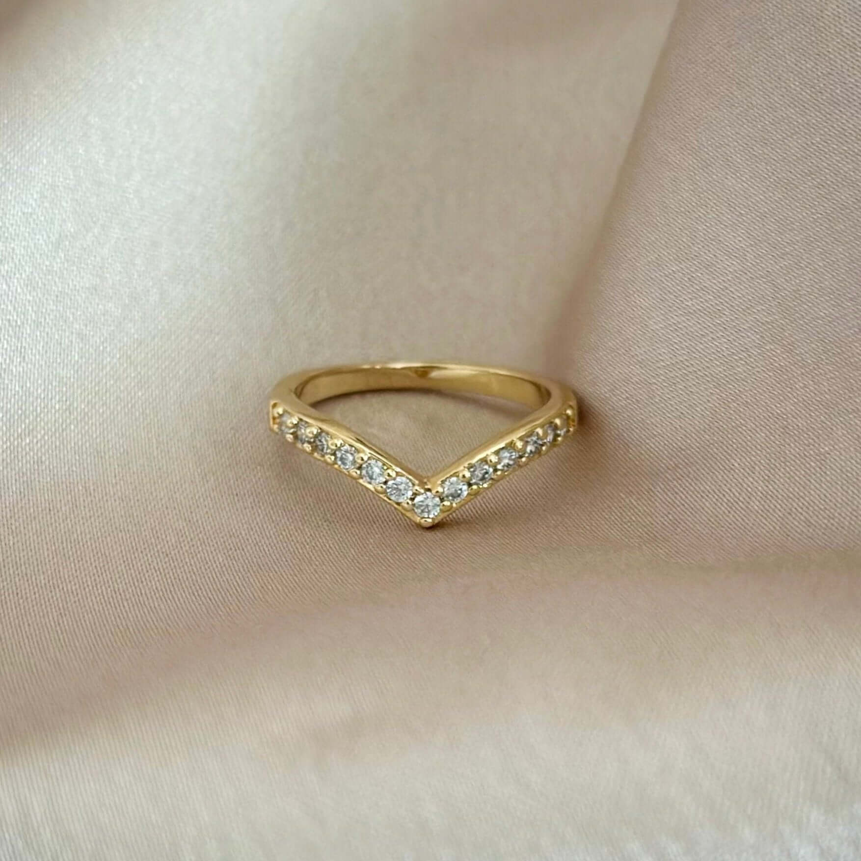 The Pave´ Peak Stacking Ring, a gold V-shaped piece adorned with pavé diamonds, displayed on a silky beige fabric.