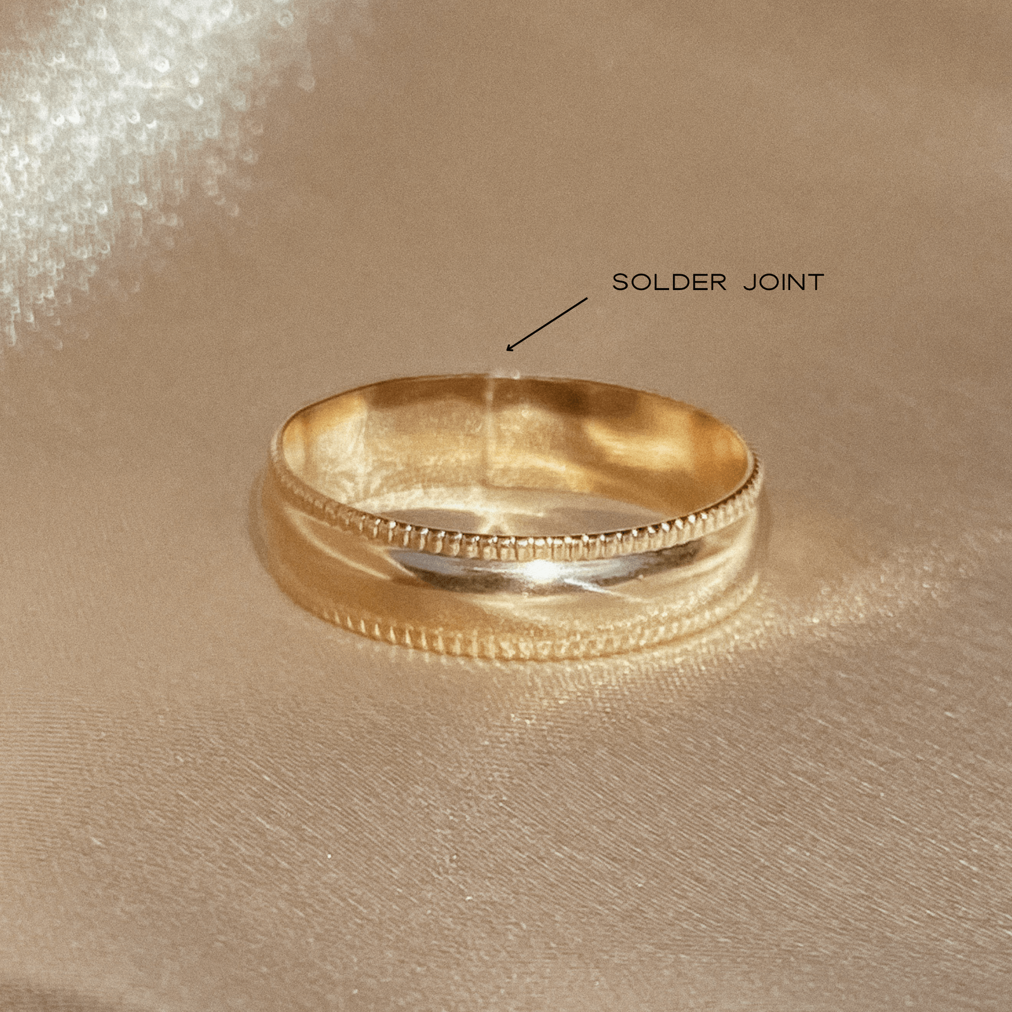 Close-up of the Selene Ring placed on fabric, highlighting its 14k gold fill with an arrow indicating the solder joint on its surface.