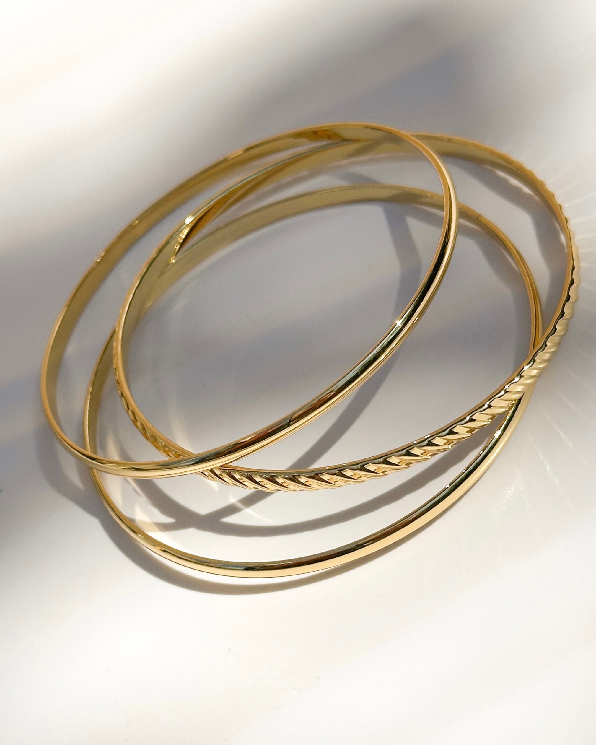 Elegant set of gold bangle bracelets displayed in soft natural light, highlighting minimalist jewelry design and polished golden finish