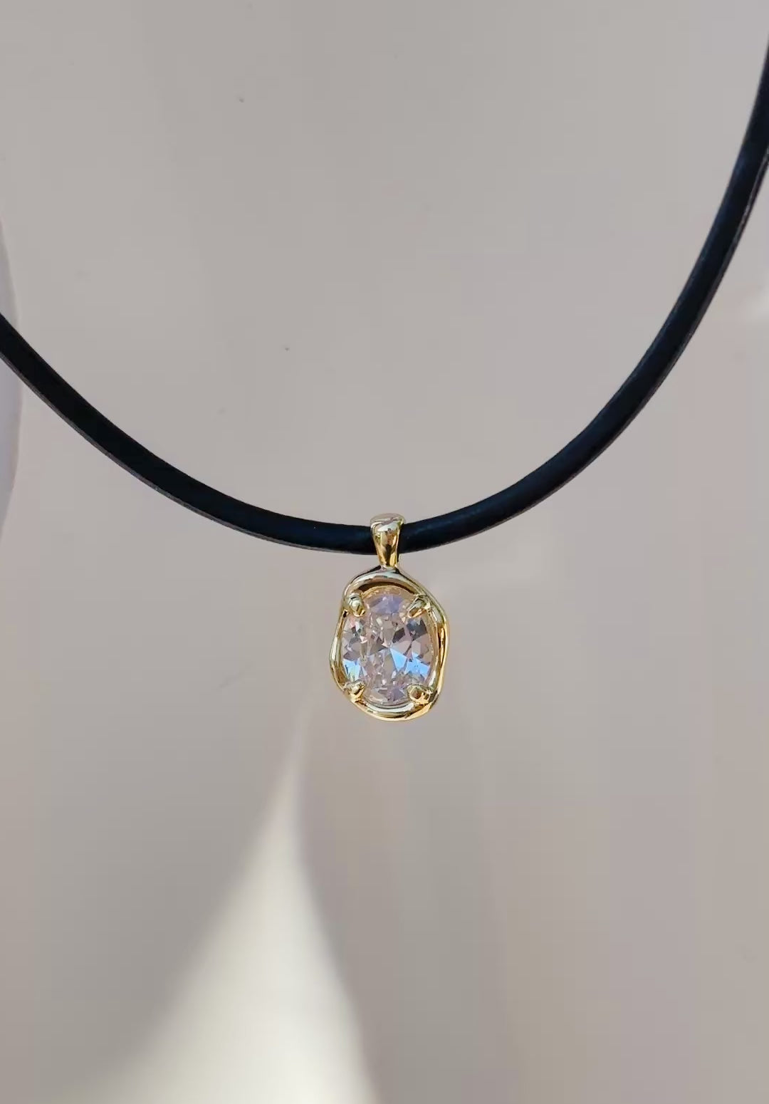 Close-up of oval stone pendant in gold bezel on black cord necklace, modern handmade jewelry