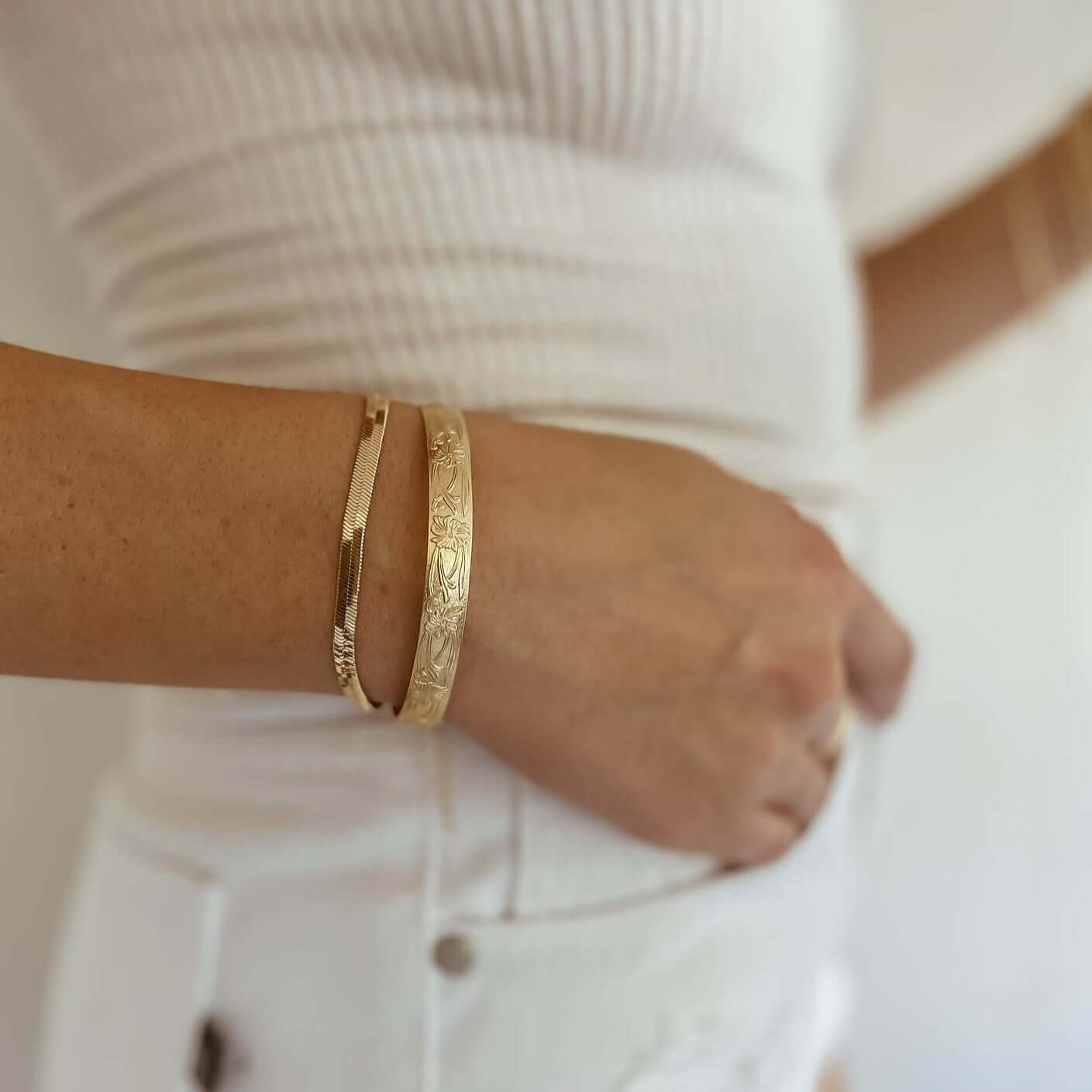 Person sporting a white tank top and white jeans, accessorized with the Marigold Cuff Bracelet and a gold bangle on their wrist.