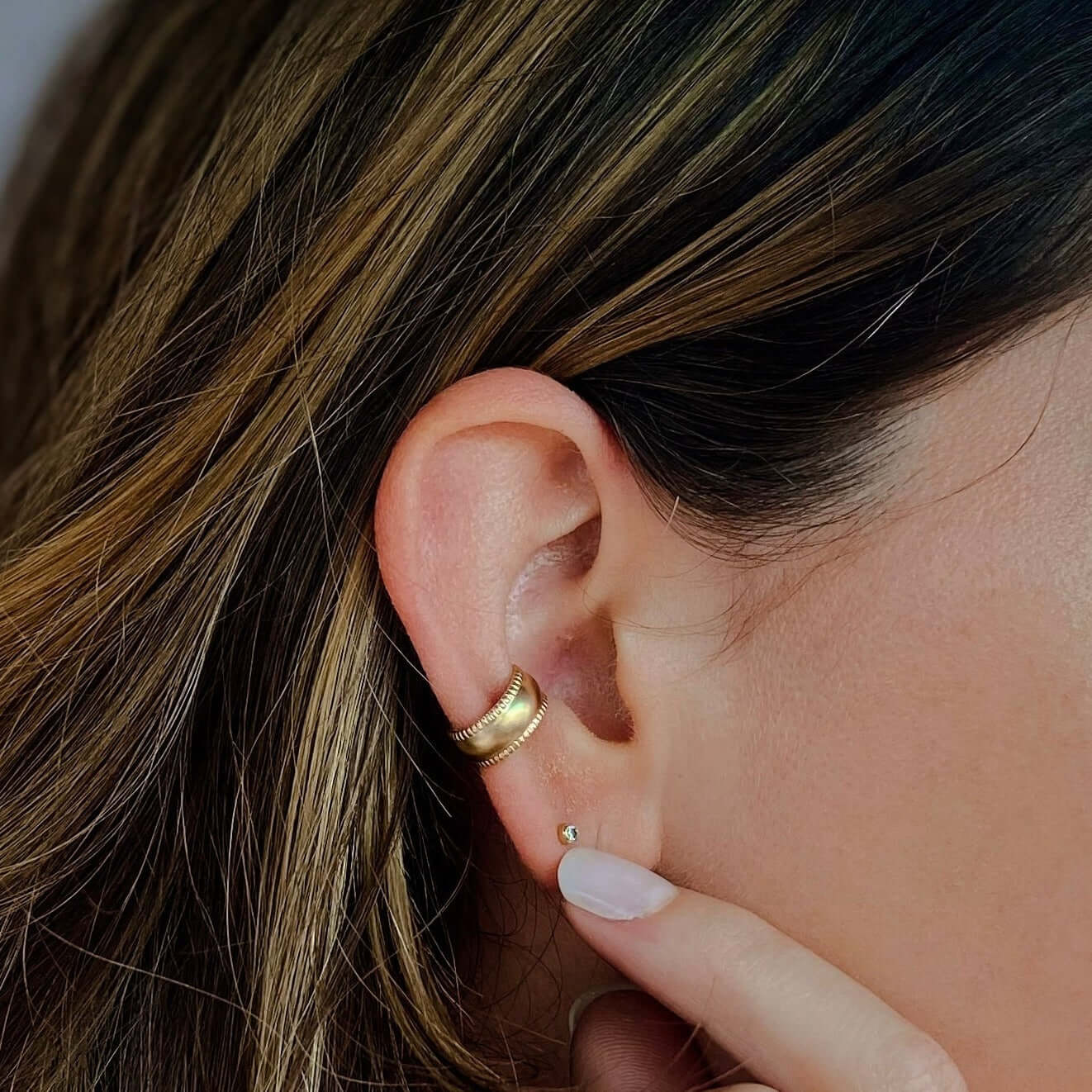 Close-up of a person's ear adorned with the Bold Ear Cuff and a small stud, fingers lightly touching the earlobe.