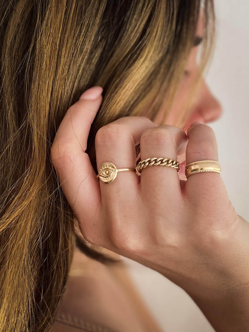 Close-up of a woman's hand adorned with multiple gold rings, featuring the Selene Ring in 14k gold fill, with her face partially visible in the background.