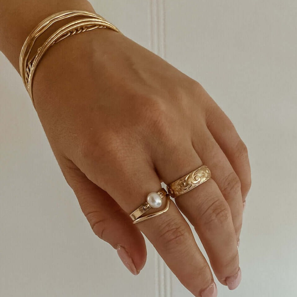 A hand wearing gold rings and bracelets, including the stunning Bold Pearl Ring, which is a 14k gold fill statement piece featuring a freshwater pearl.