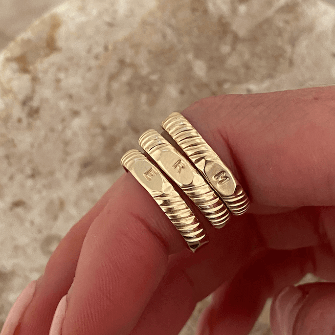 Close-up of a hand wearing four Initial Signet Rings, each made from 14k gold filled material and engraved with individual letters: E, R, I, and N.