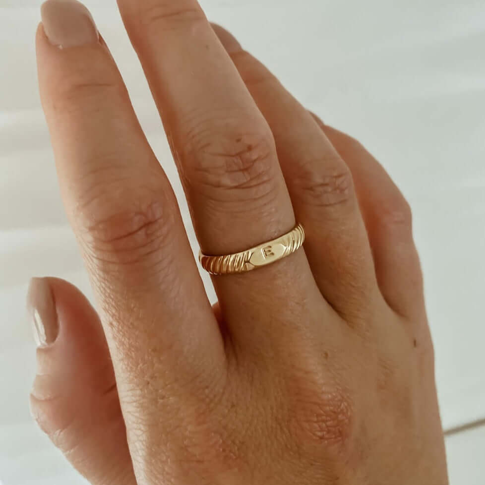 Hand with an Initial Signet Ring on the ring finger, showing a subtle design. Nails are painted in a neutral color.