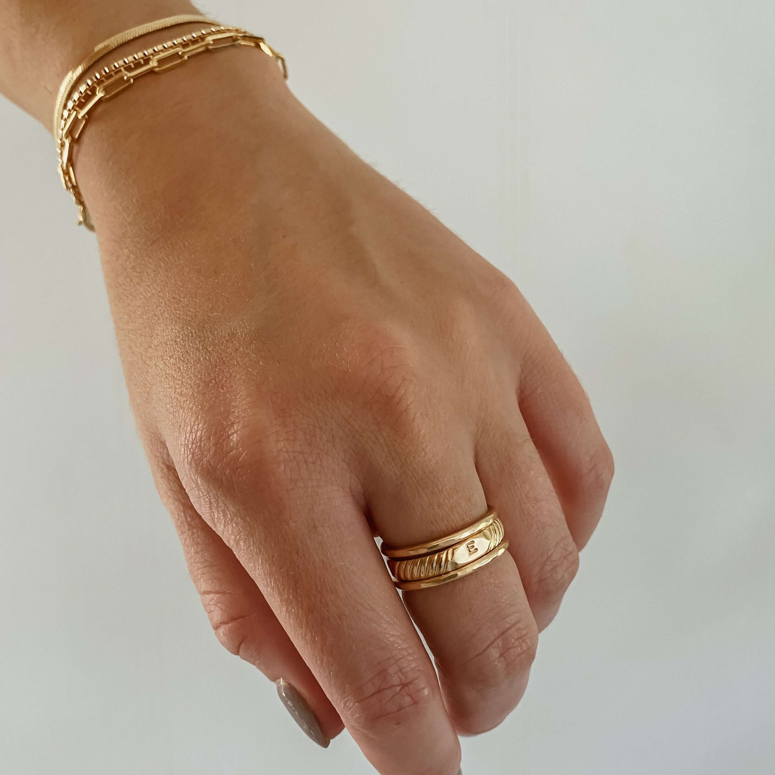 Close-up of a person's hand wearing the Initial Signet Ring made from textured 14k gold-filled material, featuring a small central diamond, and paired with a matching gold bracelet.