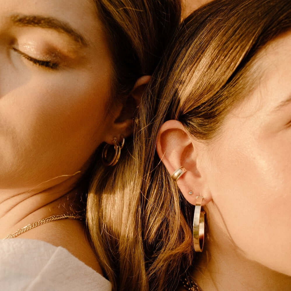 Two women with closed eyes, wearing gold hoop and stud earrings, lying close to each other.