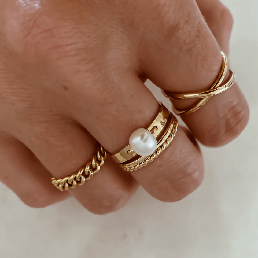 A hand wearing multiple statement rings made of 14k gold fill, including the Bold Pearl Ring adorned with a freshwater pearl, another with a chain design, and a twisted band.